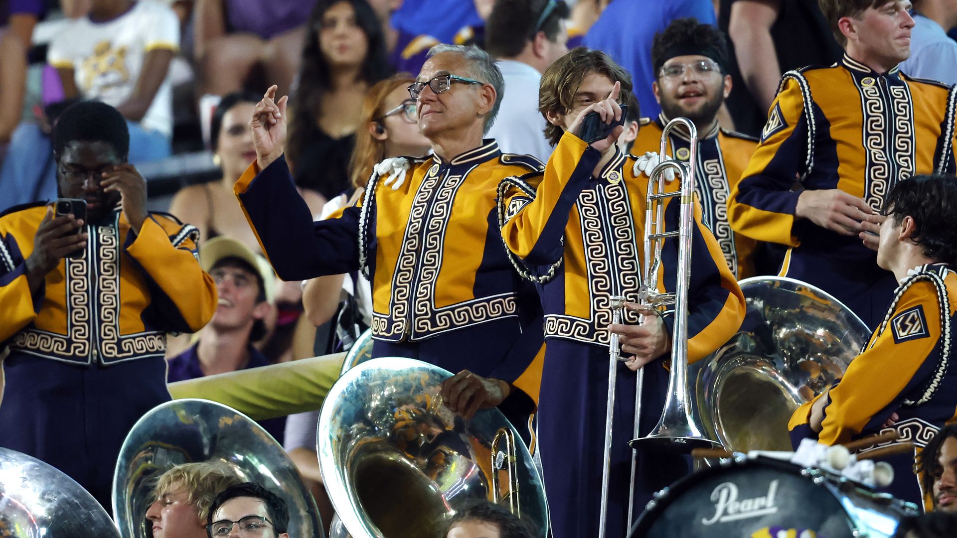 A group of diverse people wear Tiger Band uniforms and hold brass instruments.
