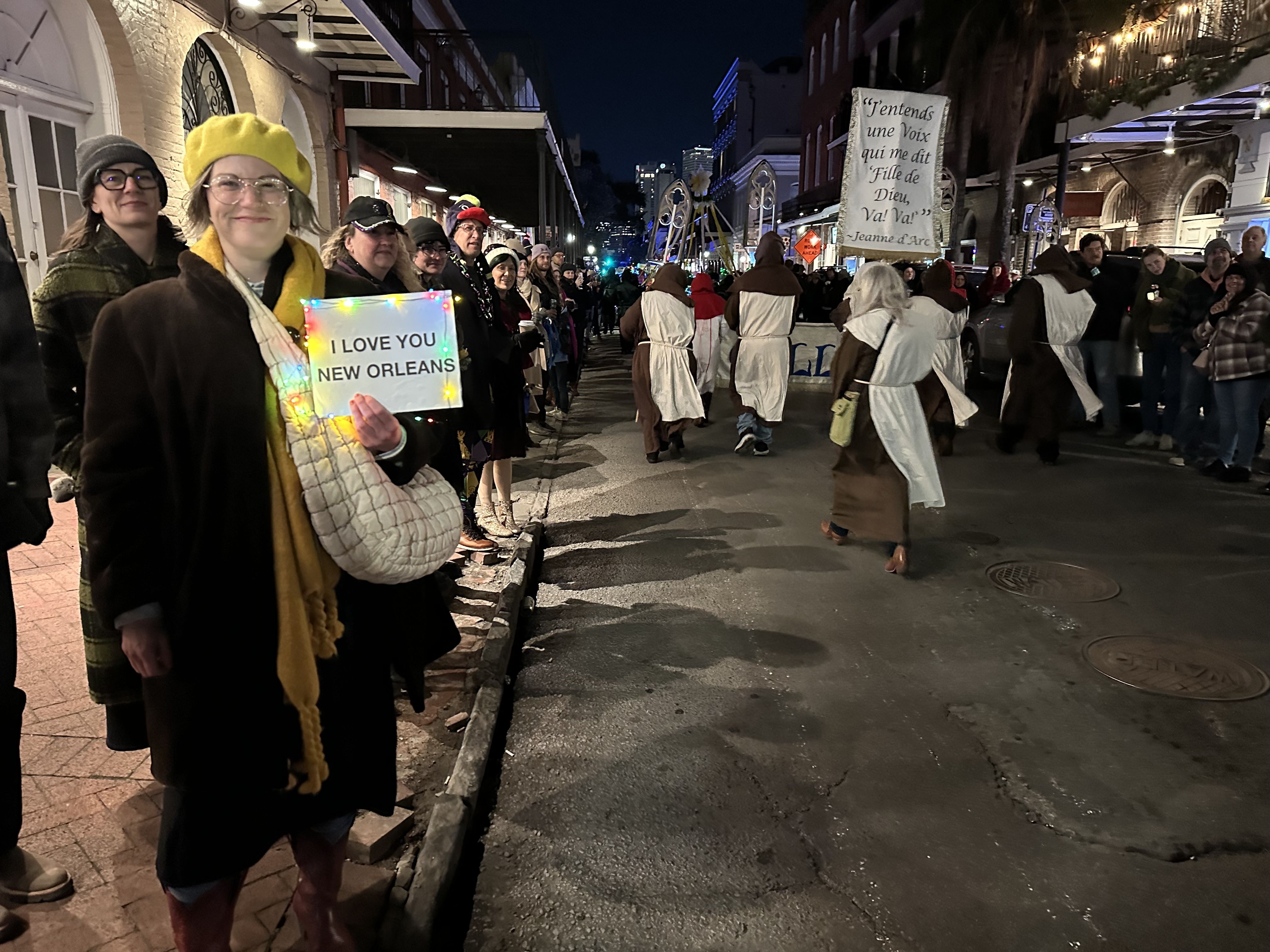 A woman holds up a sign that says "I love you New Orleans" as a parade passes behind her.