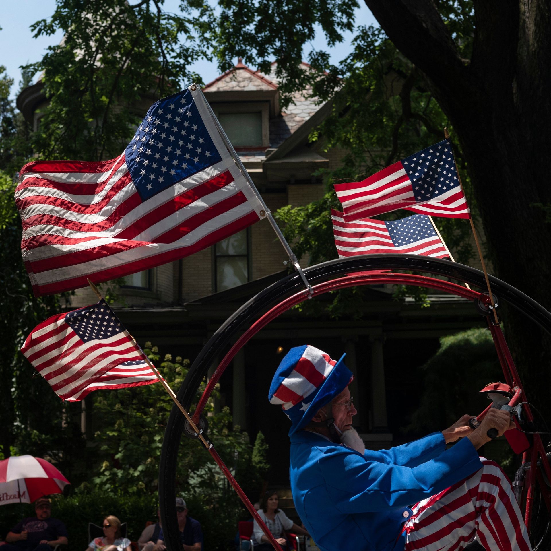 A man dressed as Uncle Sam rides a flag-adorned bicycle in a parade. 