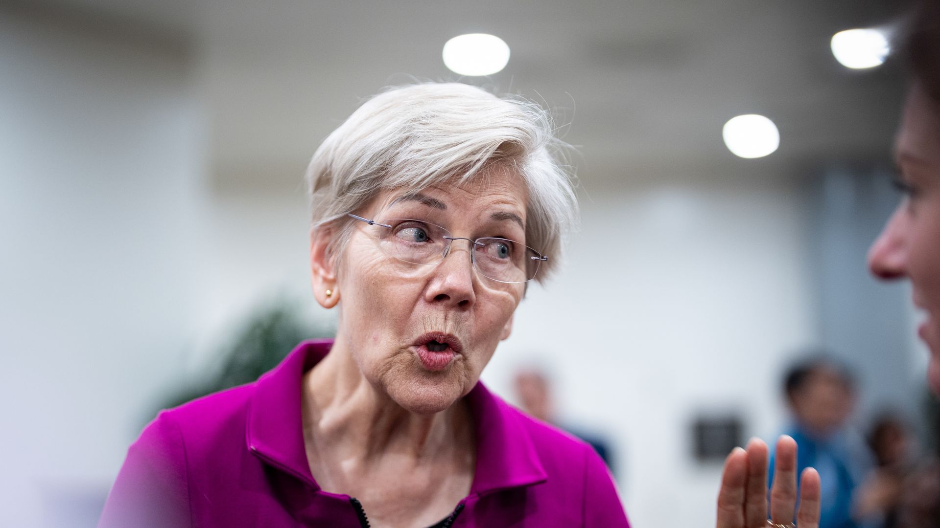 Sen. Elizabeth Warren raises a hand while talking with reporters.