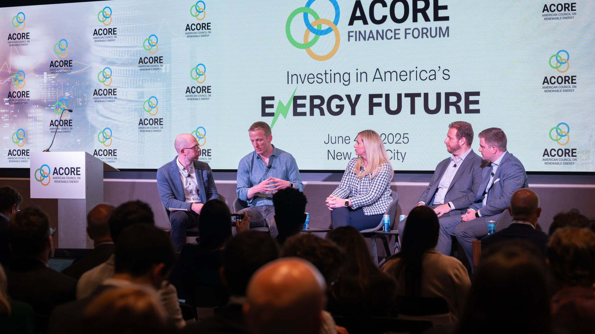 Five people sit on a stage in front of a white banner at the ACORE Finance Forum.