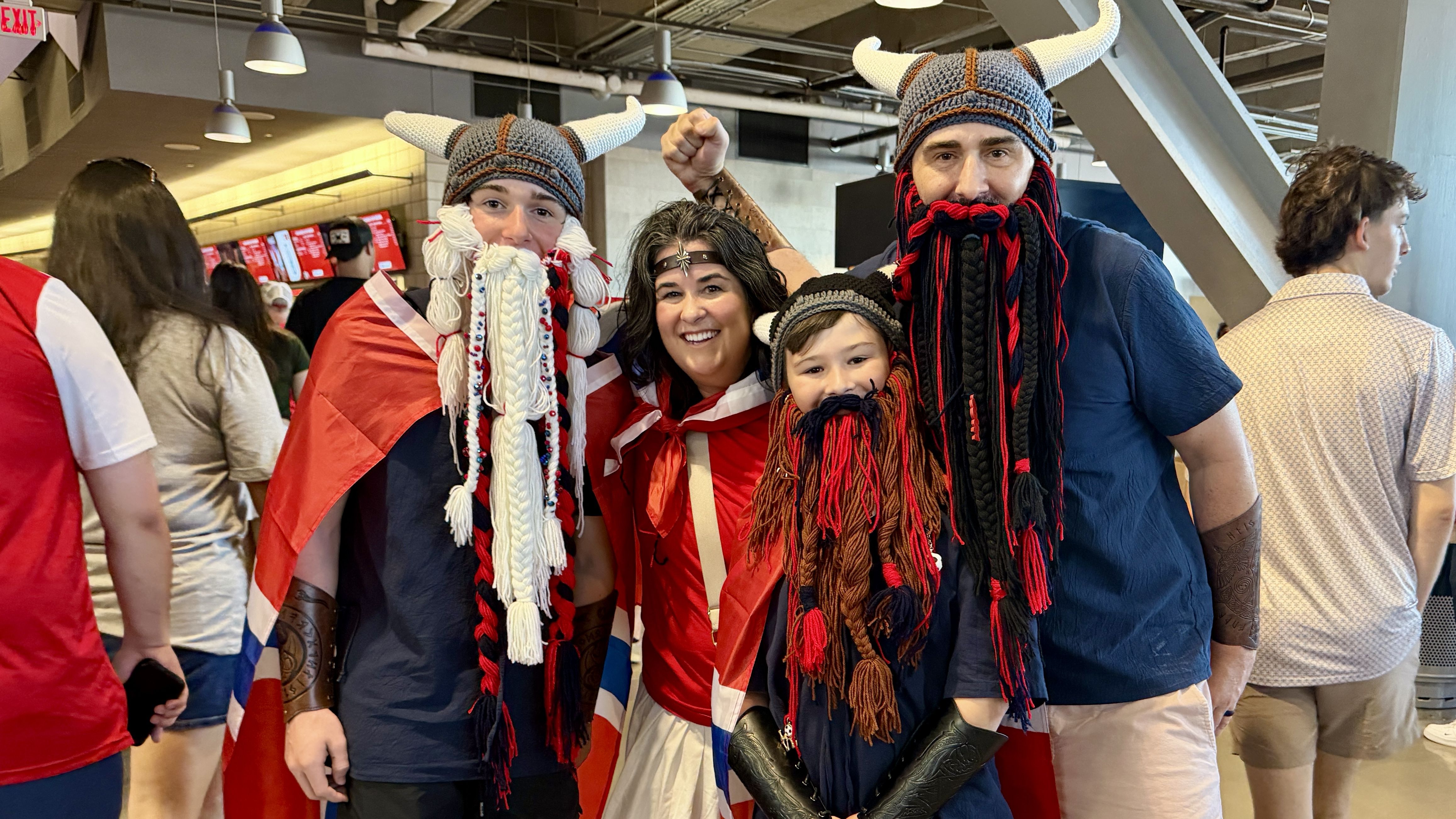 A family poses wearing red Norway gear and fake beards made of long yarn