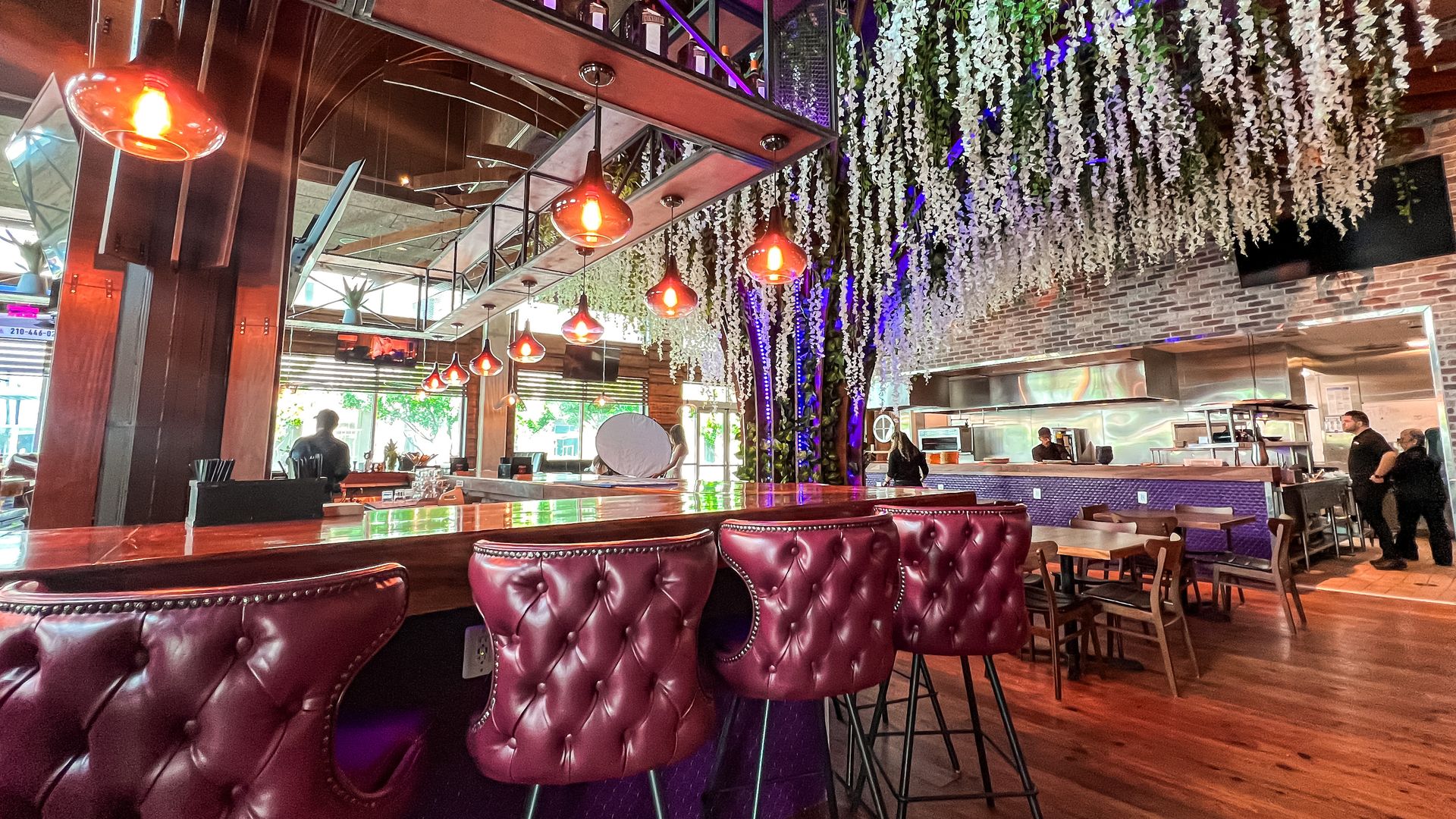 A bar with red leather high-top seats and a purple and white ceiling artwork hanging down.