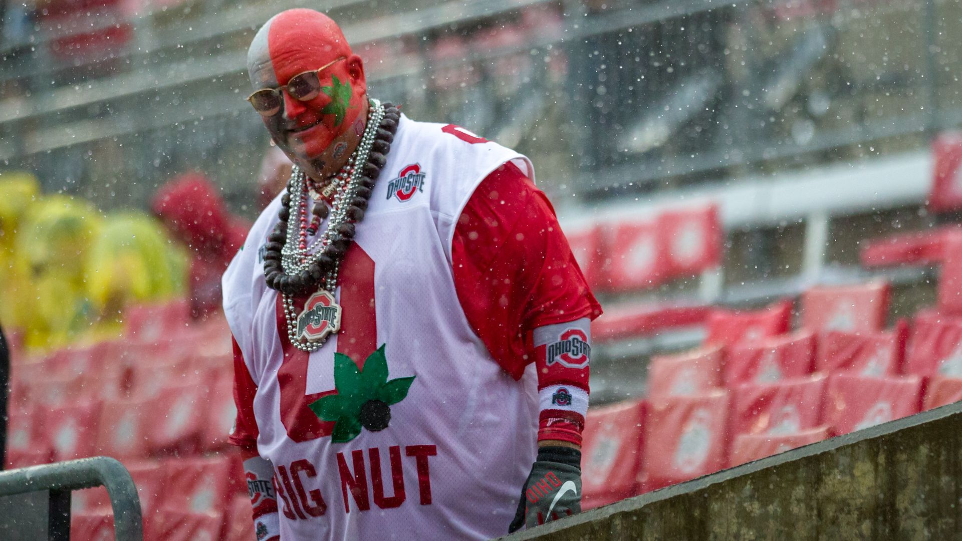 Ohio State football fan with scarlet and gray face paint, sunglasses and buckeye necklaces. 