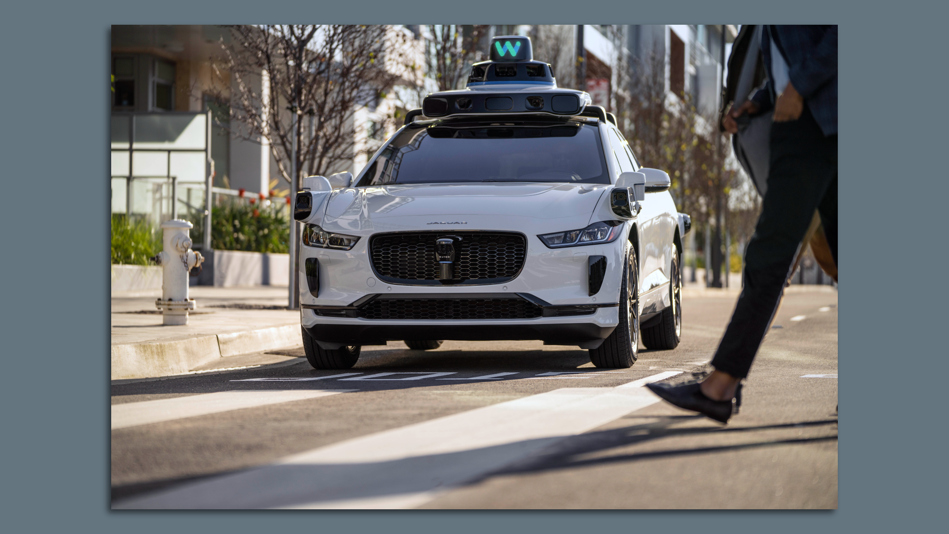 Image of a pedestrian walking in front of a driverless Waymo vehicle.
