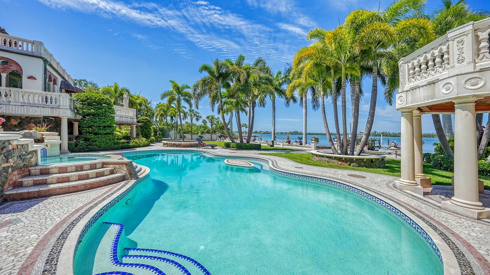 A large, lima bean-shaped backyard pool surrounded by palm trees overlooking the water.