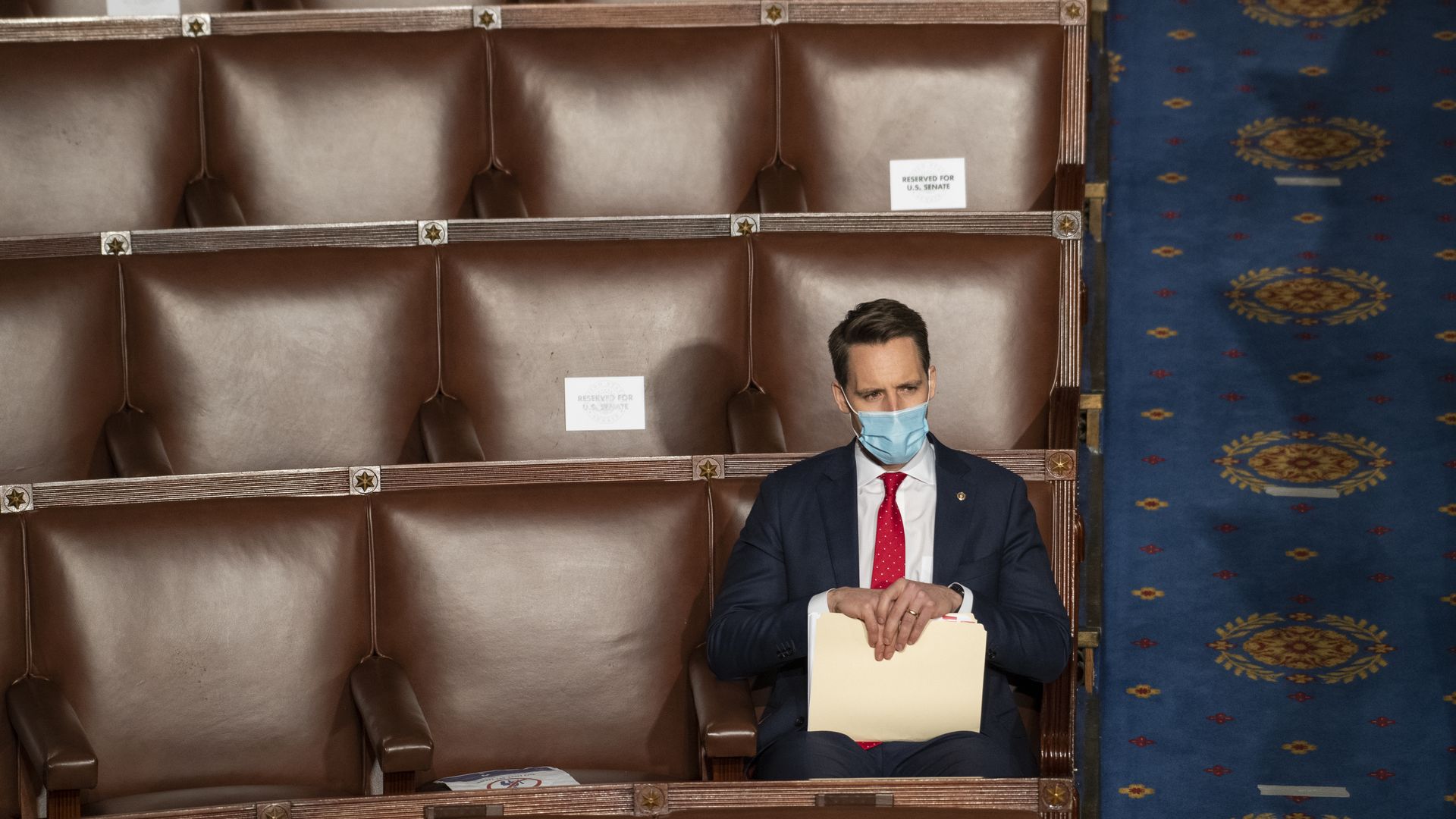 Sen. Josh Hawley sits alone with a mask on in the House chamber during the Jan. 6 vote holding a folder on his lap.