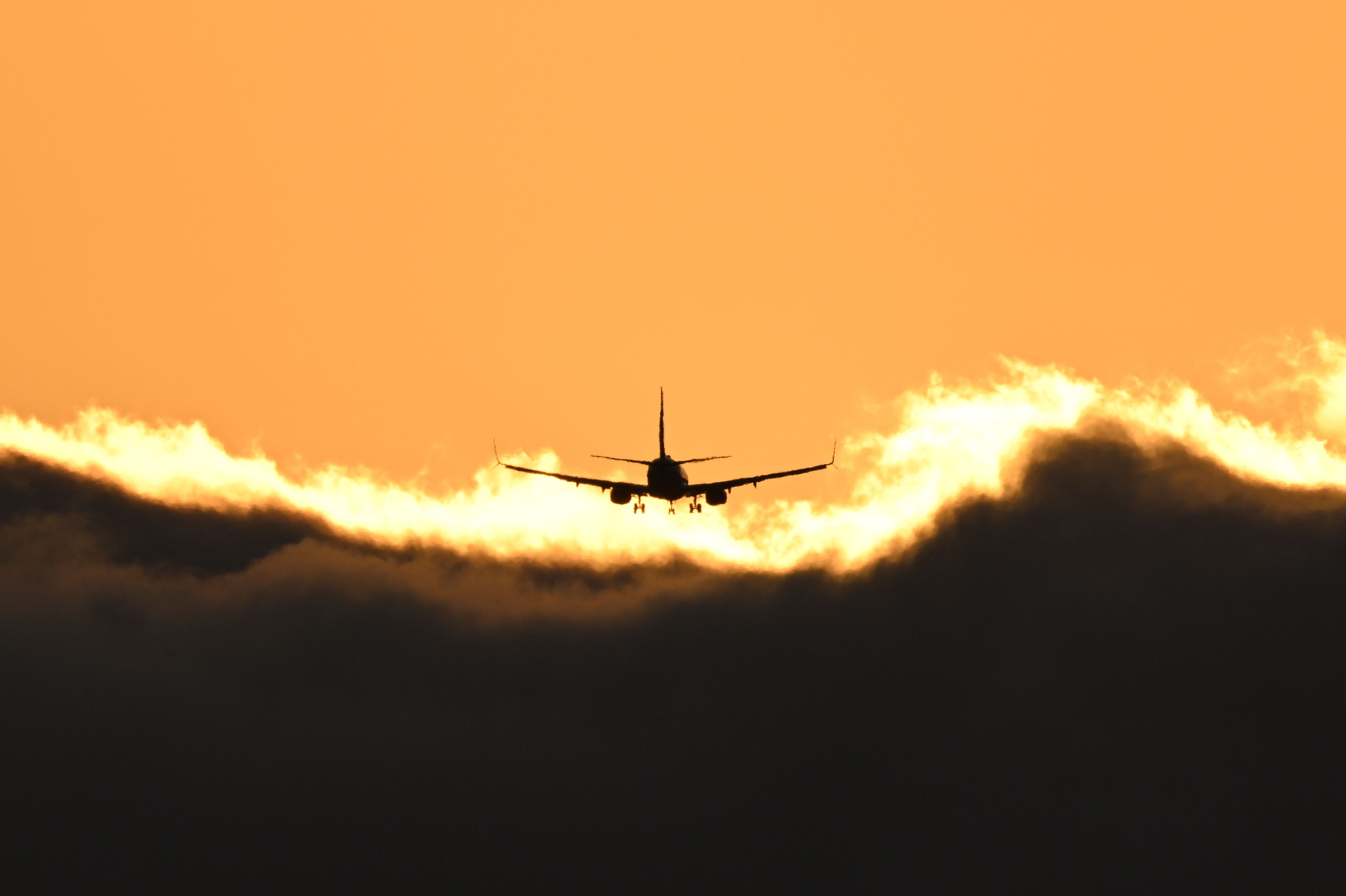 The silhouette of an airplane against an orange and yellow sunset