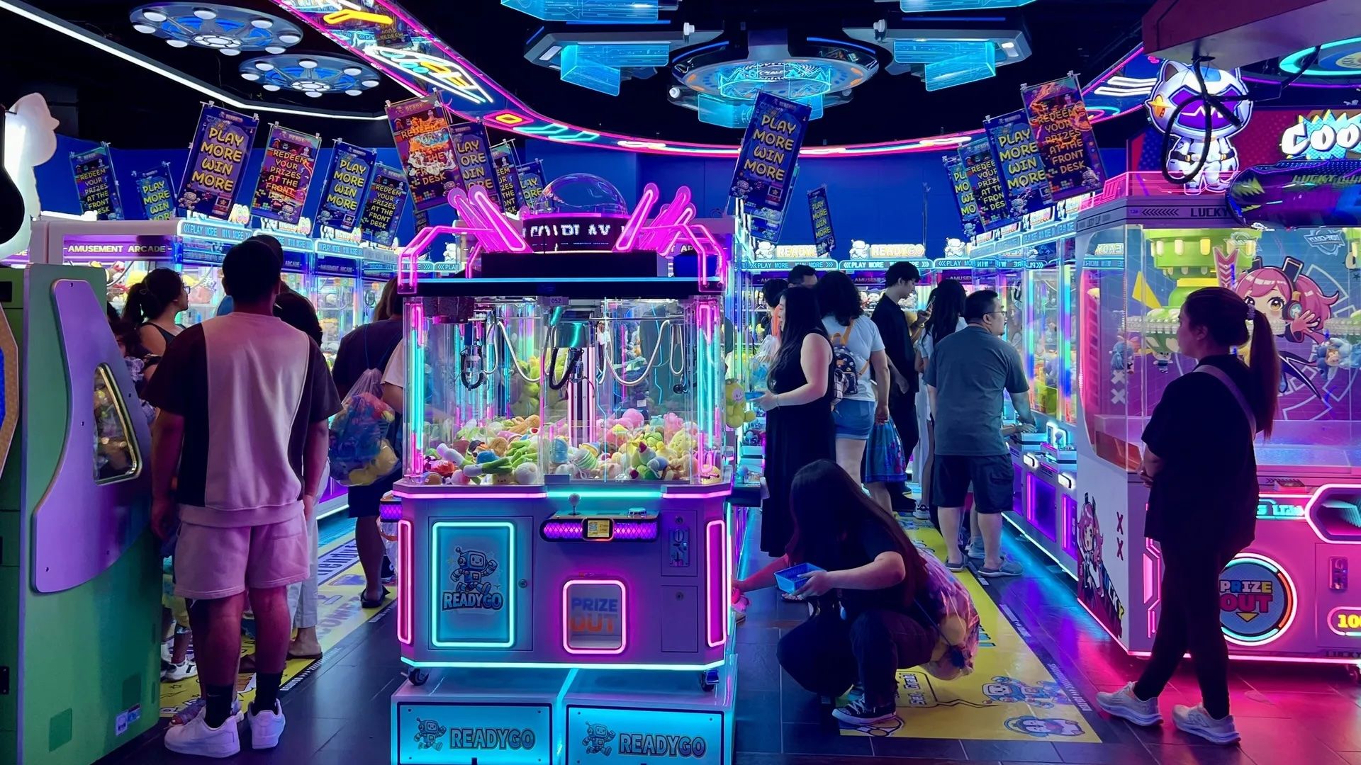 Photo of a dozen people playing claw machines.