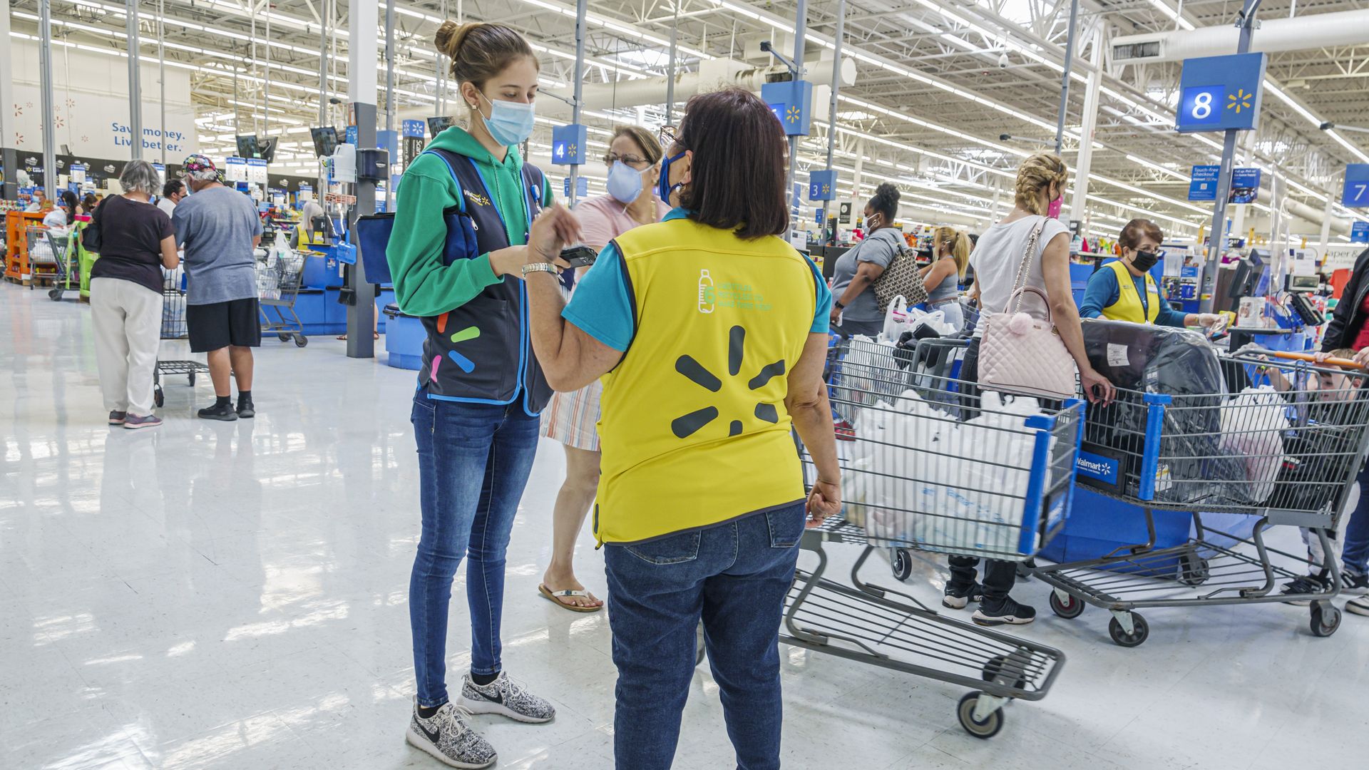 Two Walmart employees talk near full checkout counters at a store in Miami.