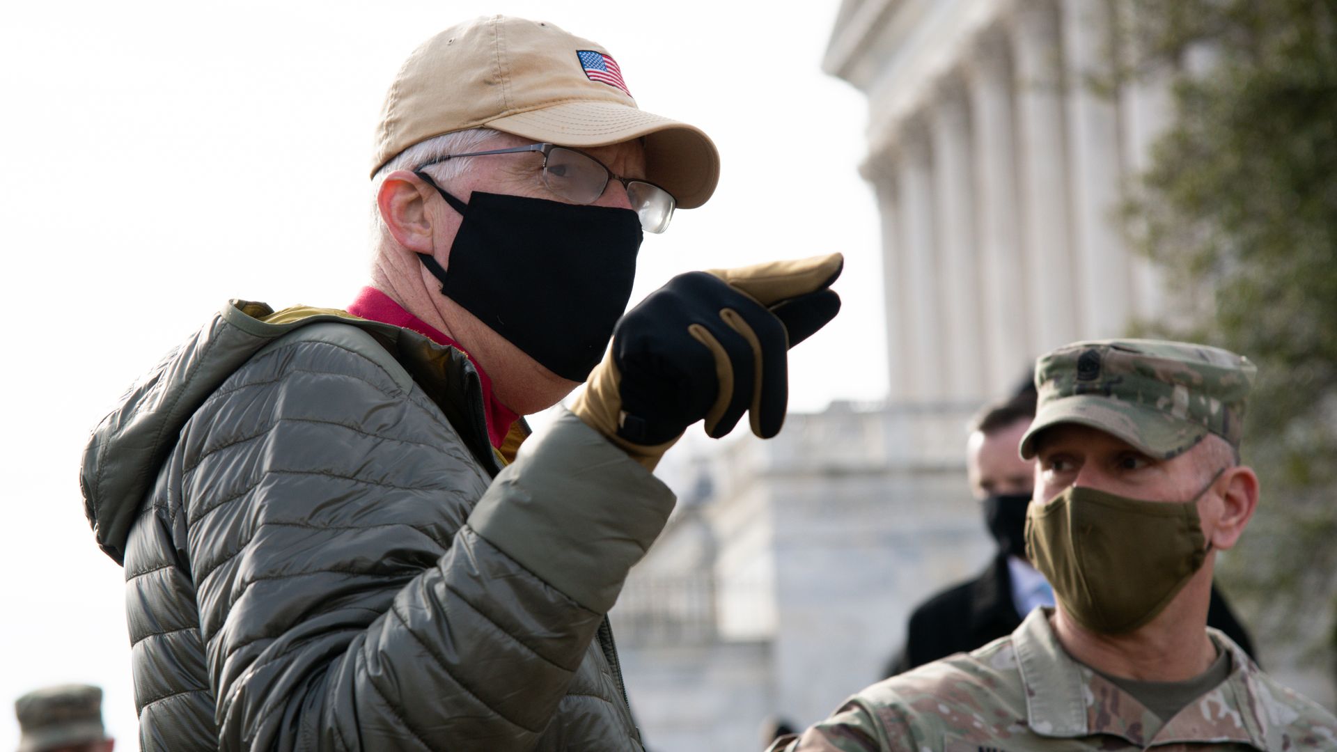 Chris Miller, wearing a face mask and a puffer jacket, points while wearing a glove