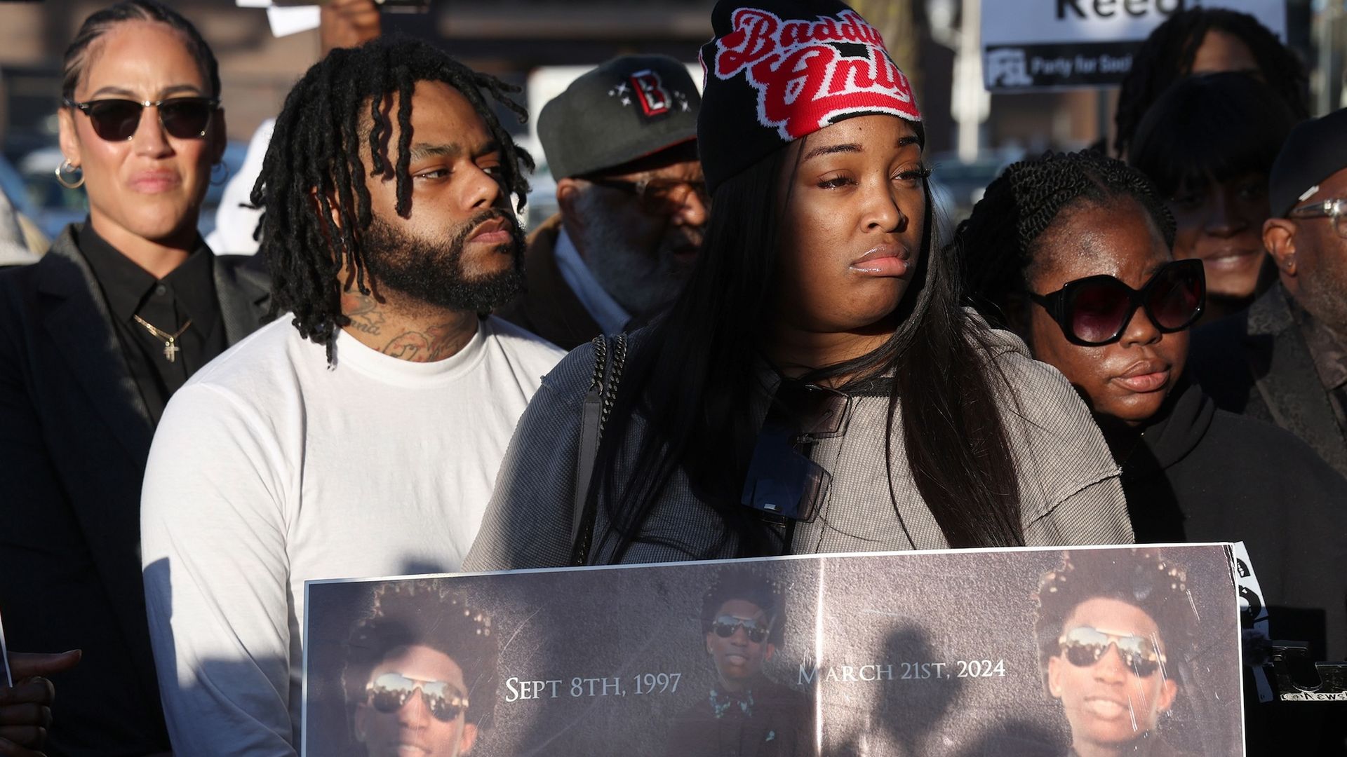 Woman holds poster with photos of Dexter Reed.