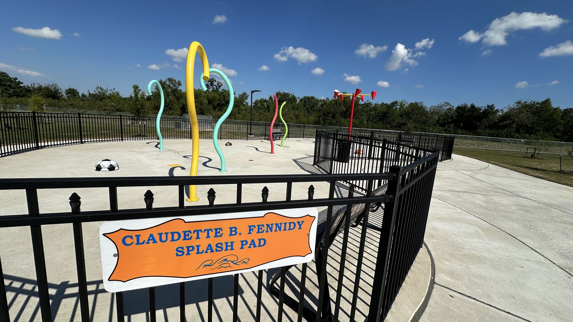 An empty splash pad is seen at midday. It is fenced in, and the water isn't turned on.