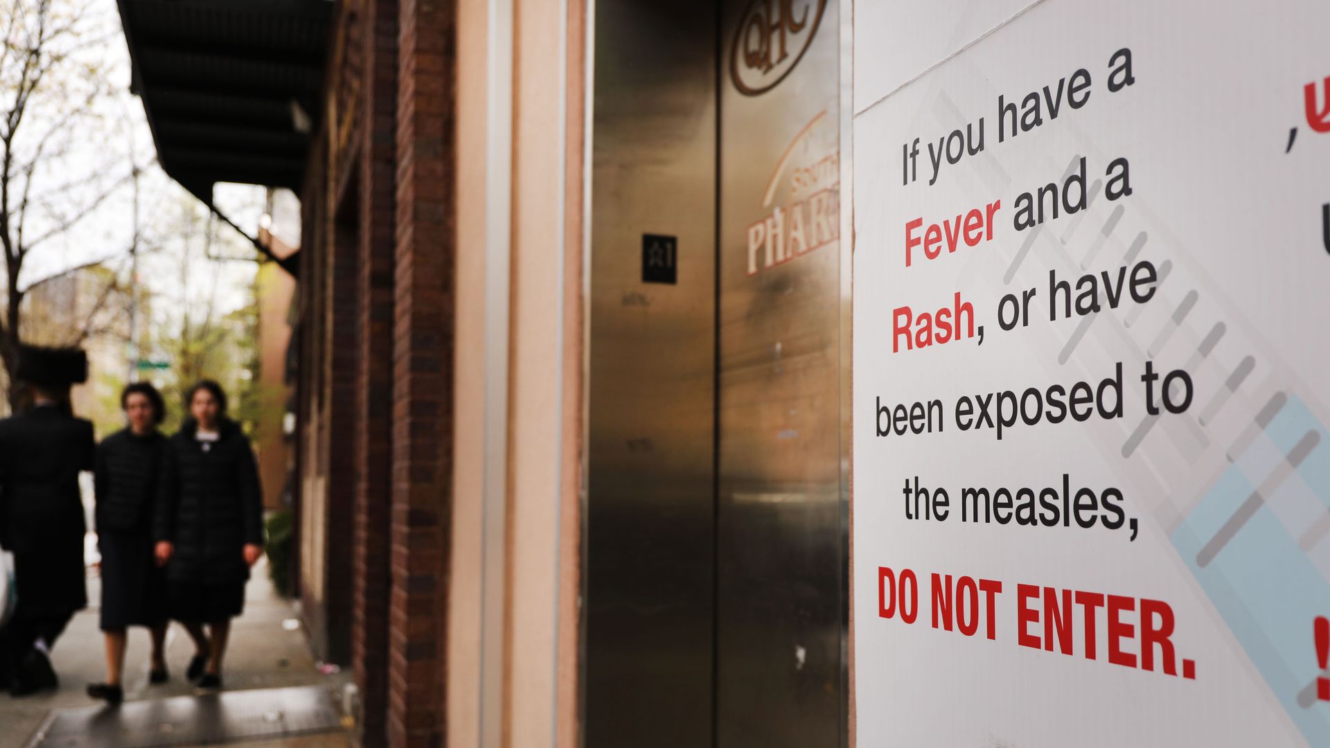 In this image, a sign posted next to an elevator reads: "If you have a fever and a rash, or have been exposed to the measles, do not enter.'