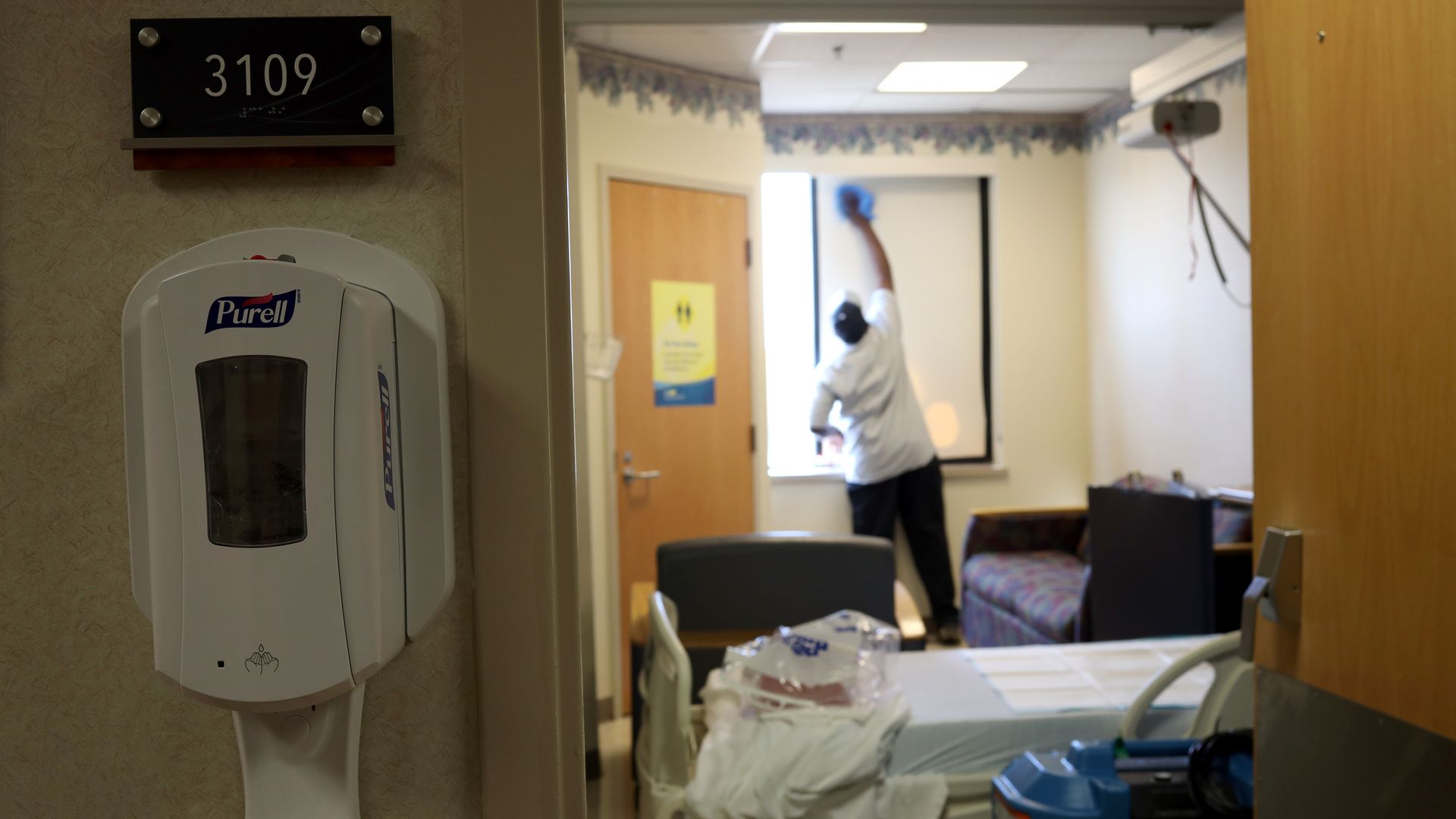 A worker cleans a hospital room while hand sanitizer is in the foreground.