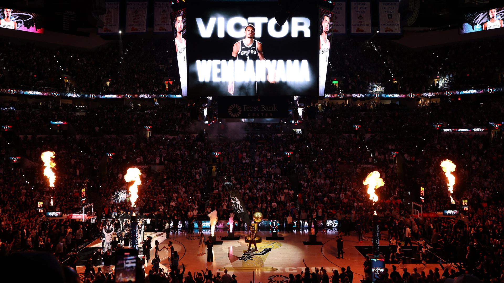 A darkened sports stadium is illuminated by fireworks and a big screen in the center with a graphic of Victor Wembanyama.