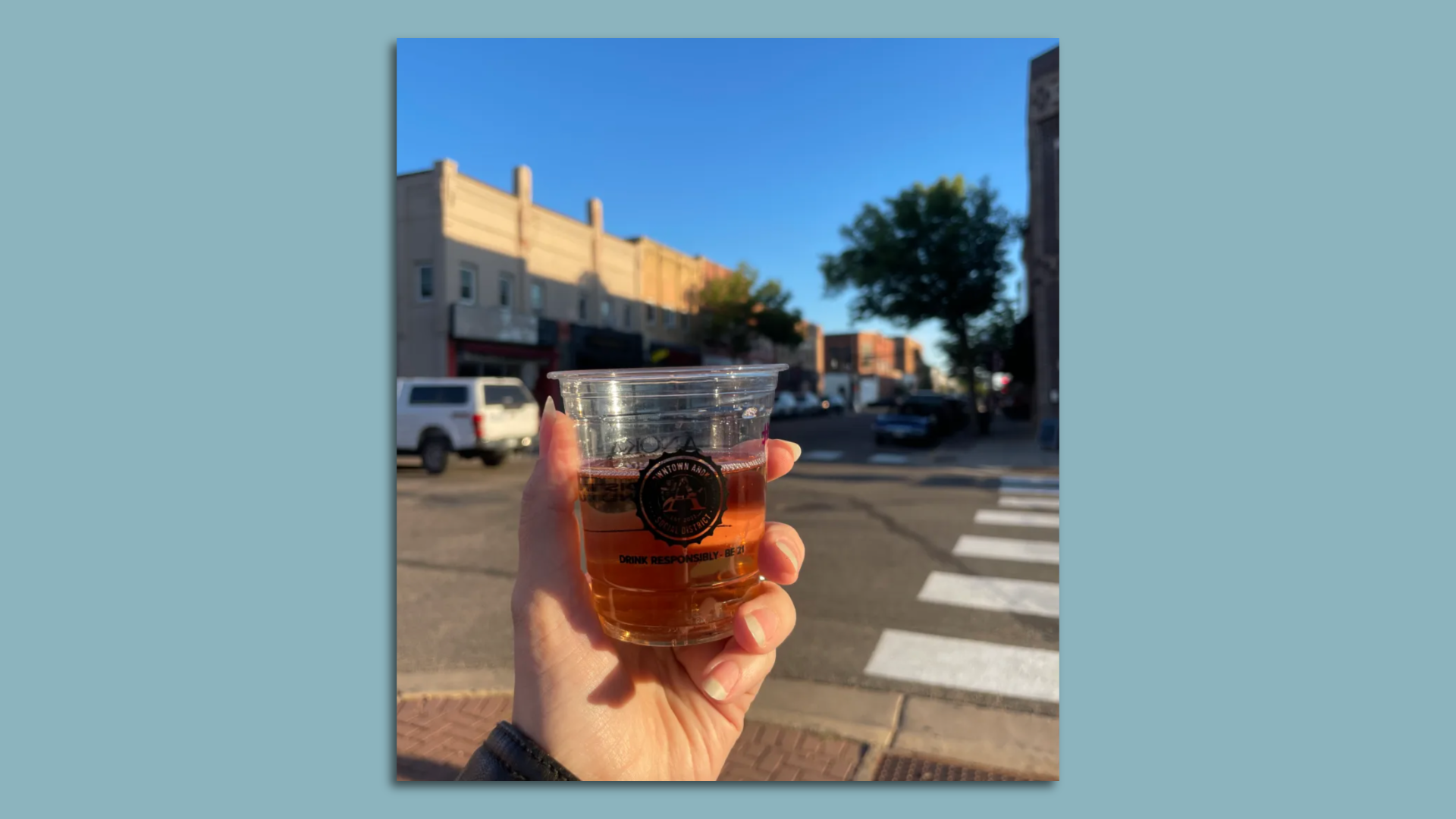 a hand holding a cup of wine on a sidewalk