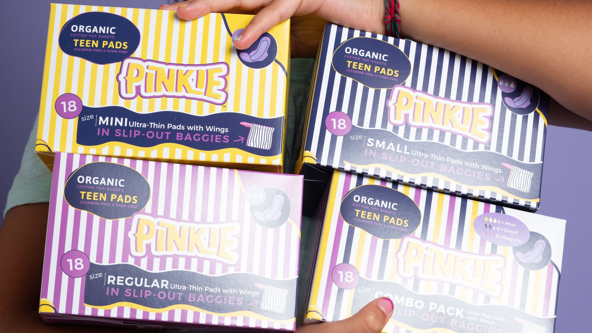 A teen girl holds four different versions of Pinkie-branded period pads.