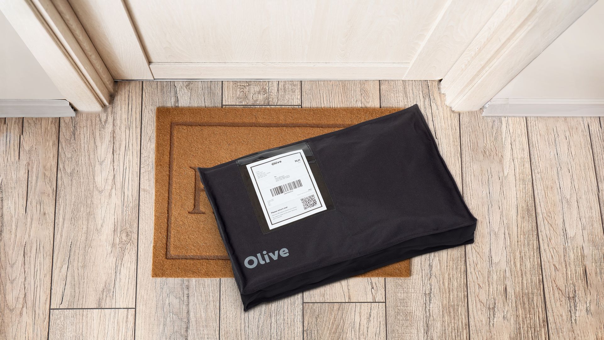 A delivery in black reusable packaging sits on a doorstep on top of a 'welcome' mat.
