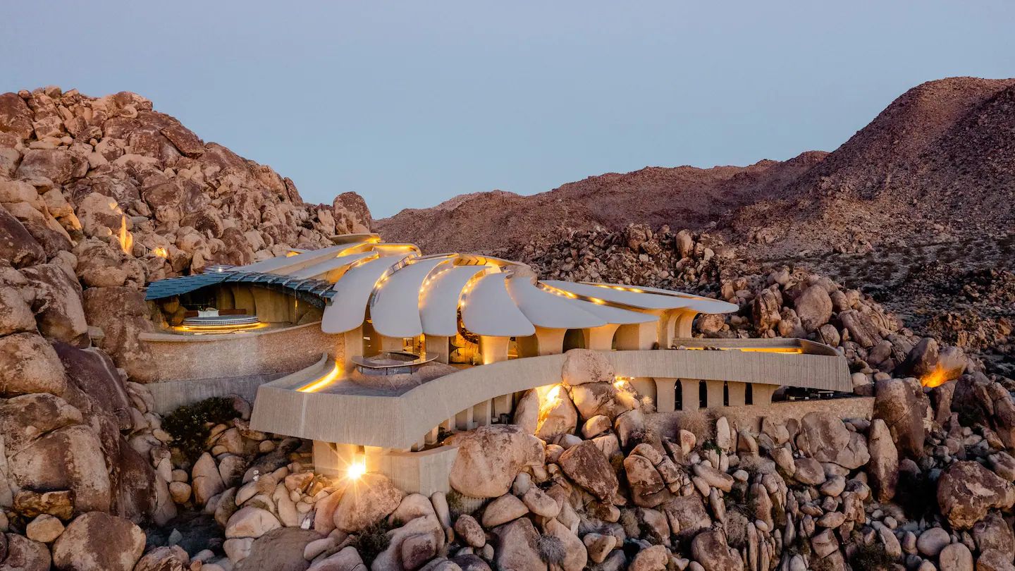 A futuristic stone-colored, multi-level home sits in rocky terrain. 
