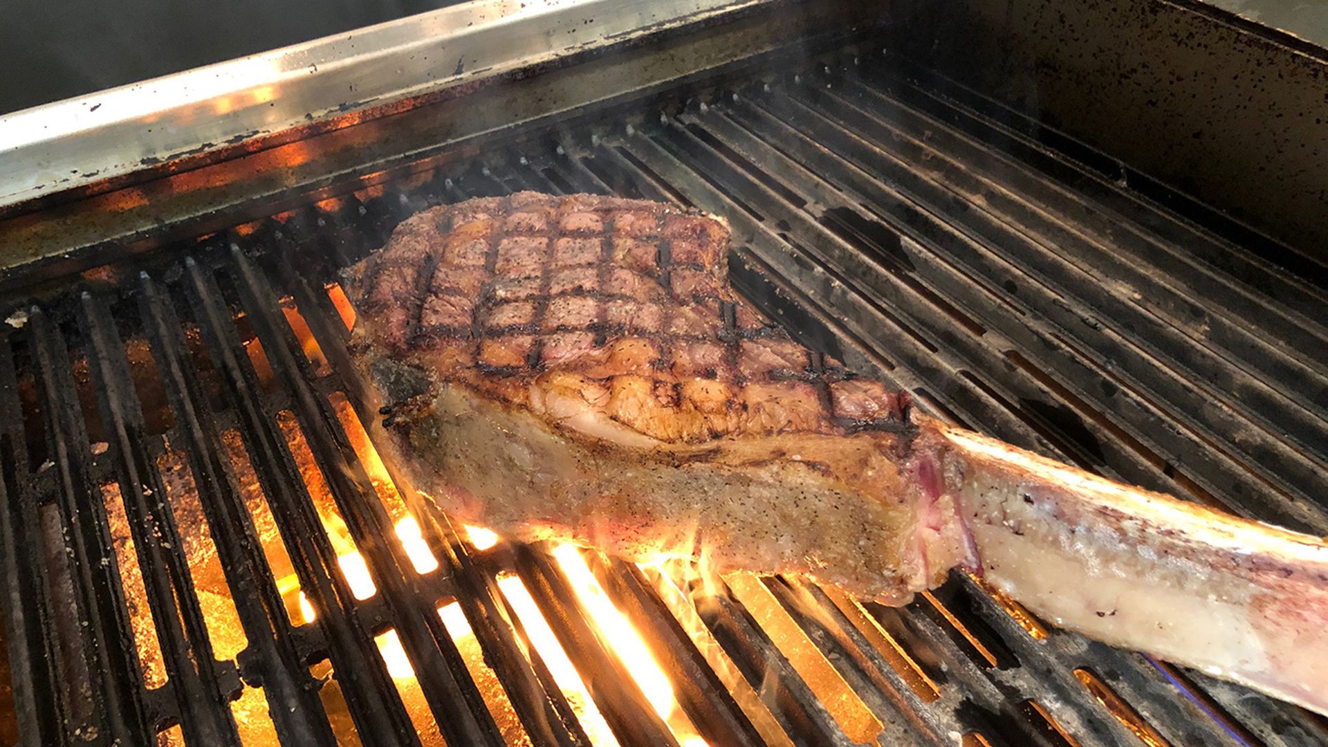 a tomahawk steak over a grill with a flame