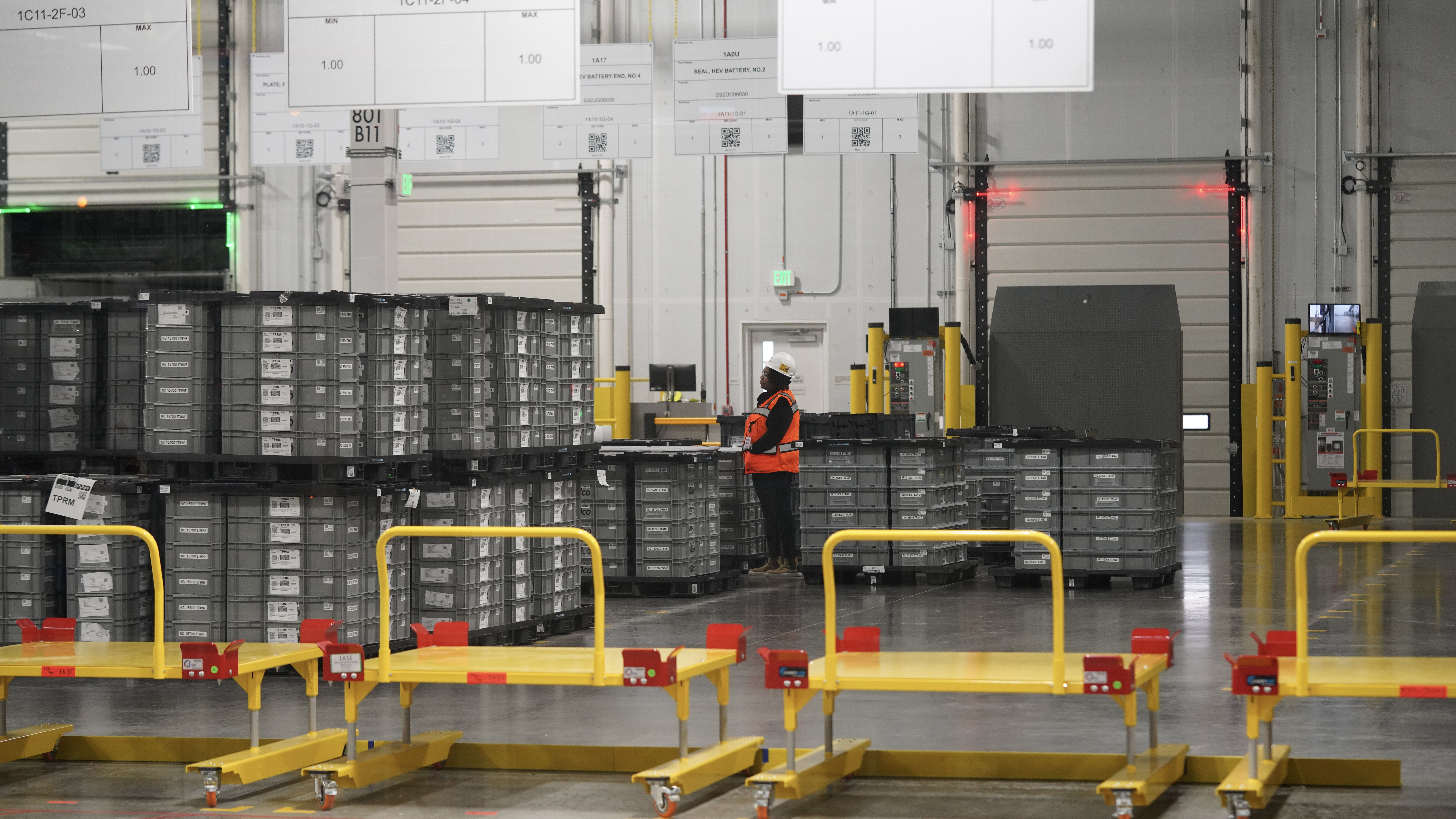 Worker in safety vest standing among stacked containers in a warehouse.