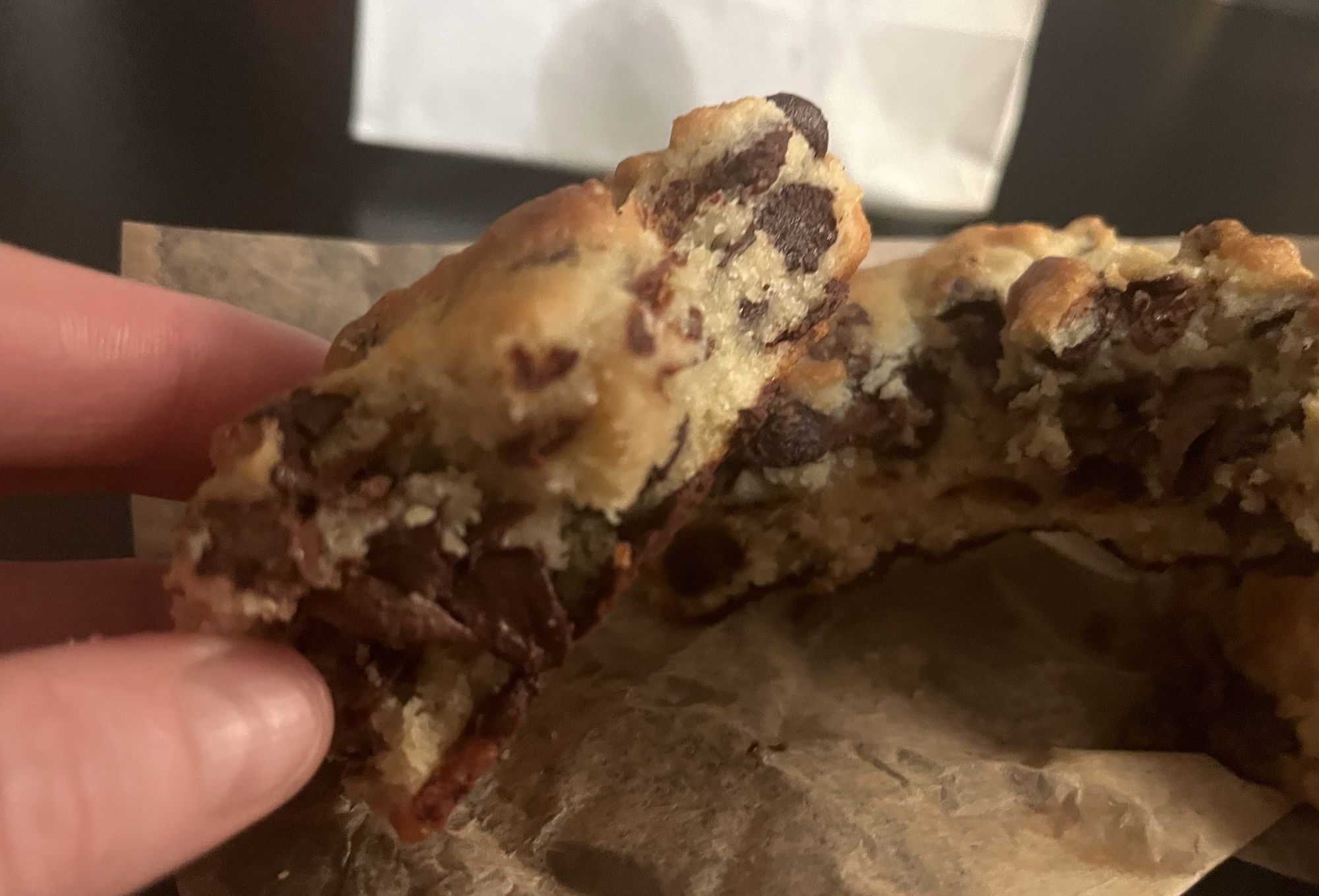 Fingers holding half of a chocolate chip cookie.