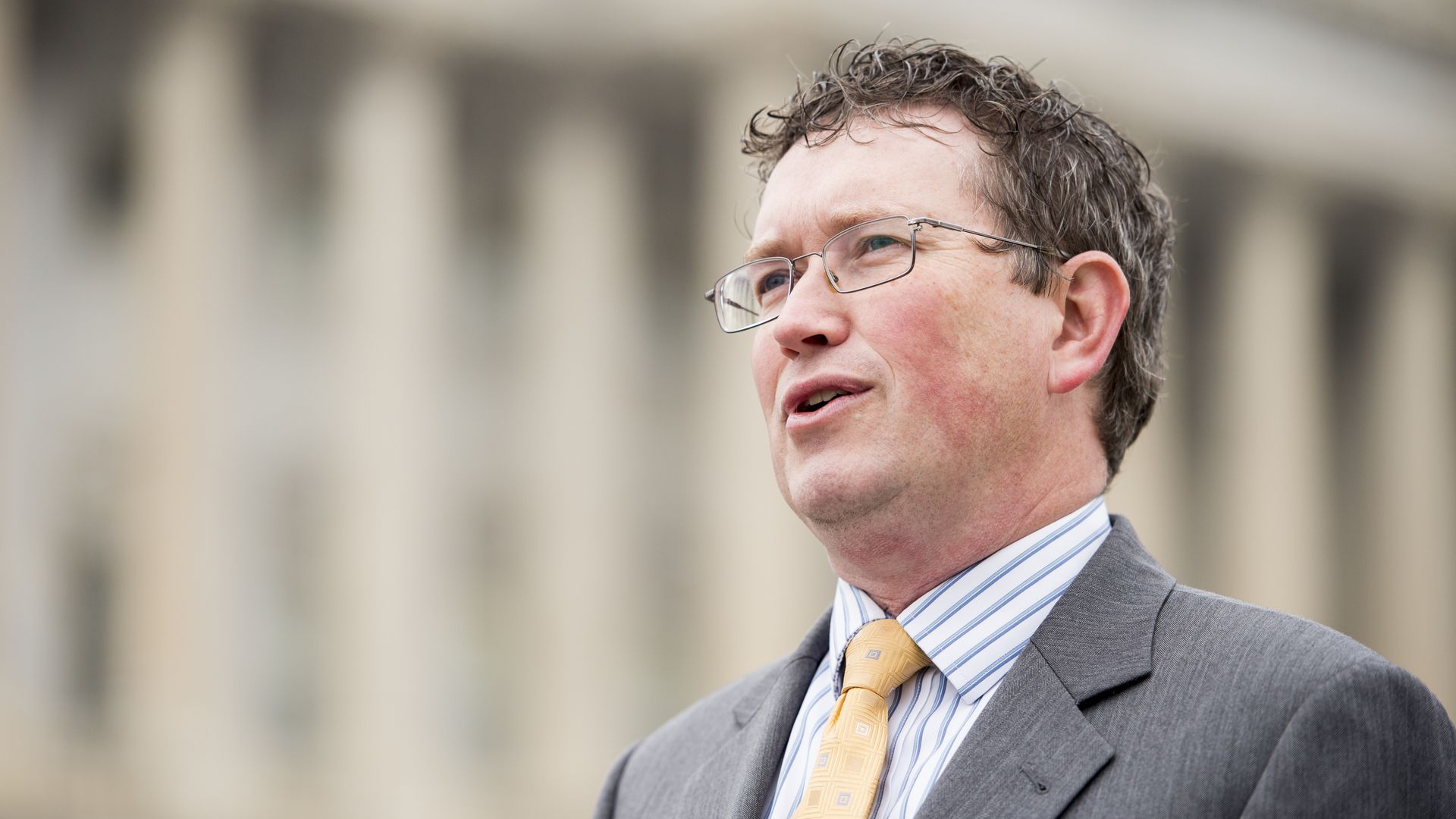 In this image, Massie stands and speaks outside in a suit.