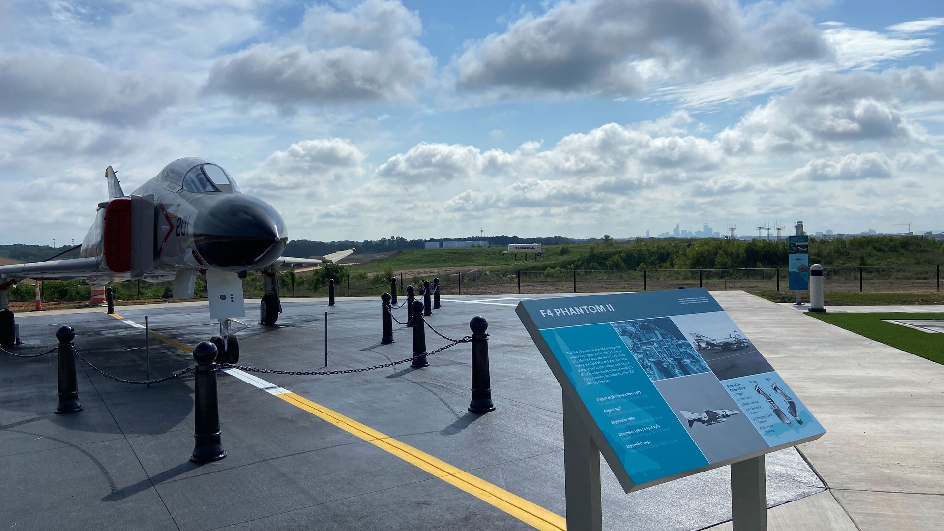 A retired U.S. military fighter jet, an F-4 Phantom II, on display at Charlotte Douglas International Airport's new airport overlook with the city skyline in the background.