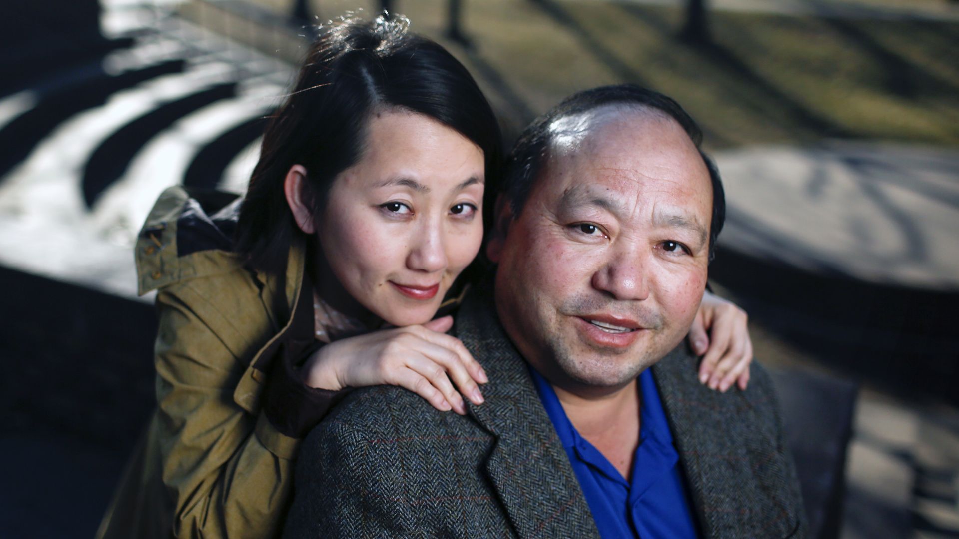 A man and a woman pose for a photograph sitting outside. Both are smiling