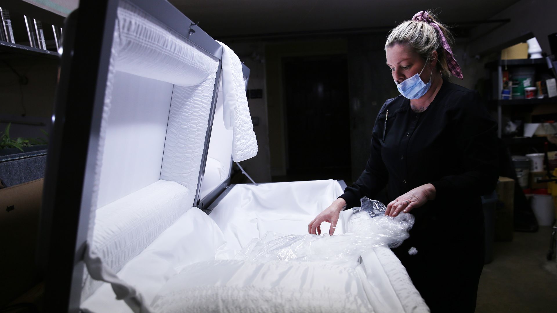 Embalmer and funeral director Kristy Oliver unwraps a new casket which will be used for a person who died after contracting COVID-19 at East County Mortuary on January 15