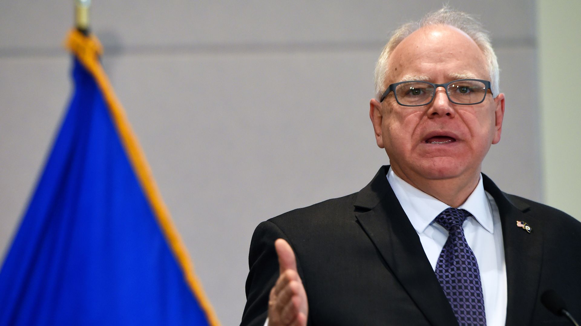 Gov. Tim Walz stands at a podium in a suit