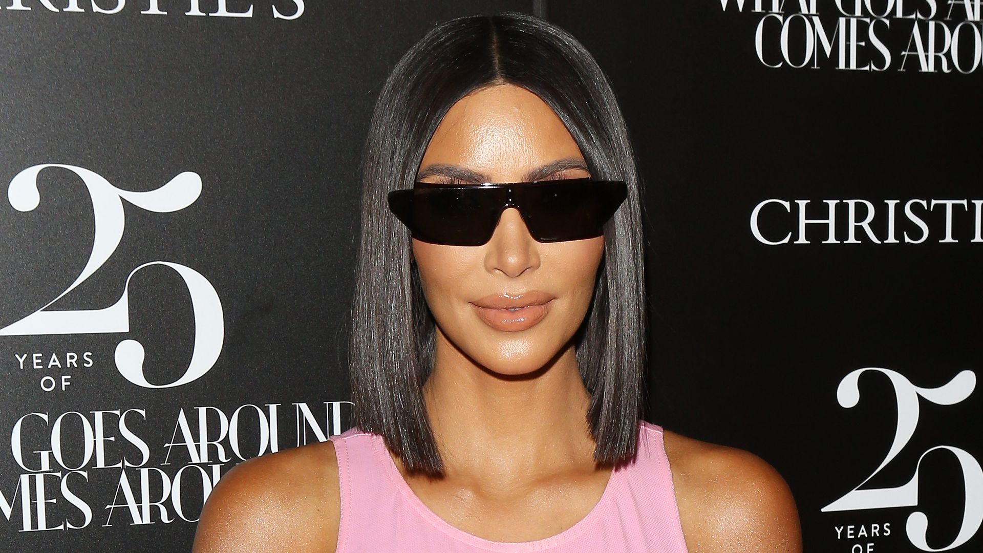 Kim Kardashian where rectangular, dark sunglasses and a light pink tank top posing for a photo seemingly on a red carpet