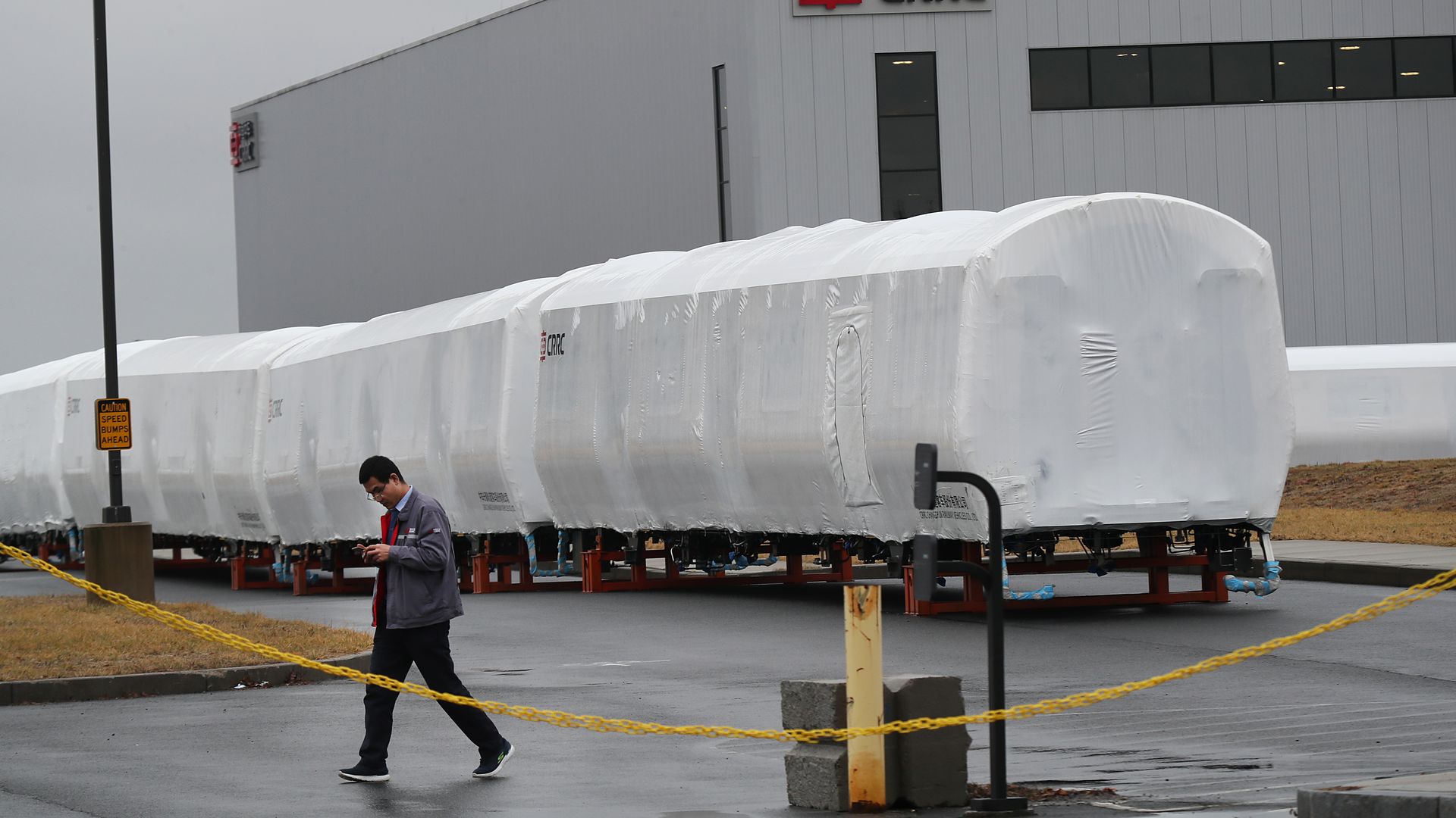 A CRRC worker walks through the company's factory lot in Springfield. Behind him, trains covered by large, white tarps.