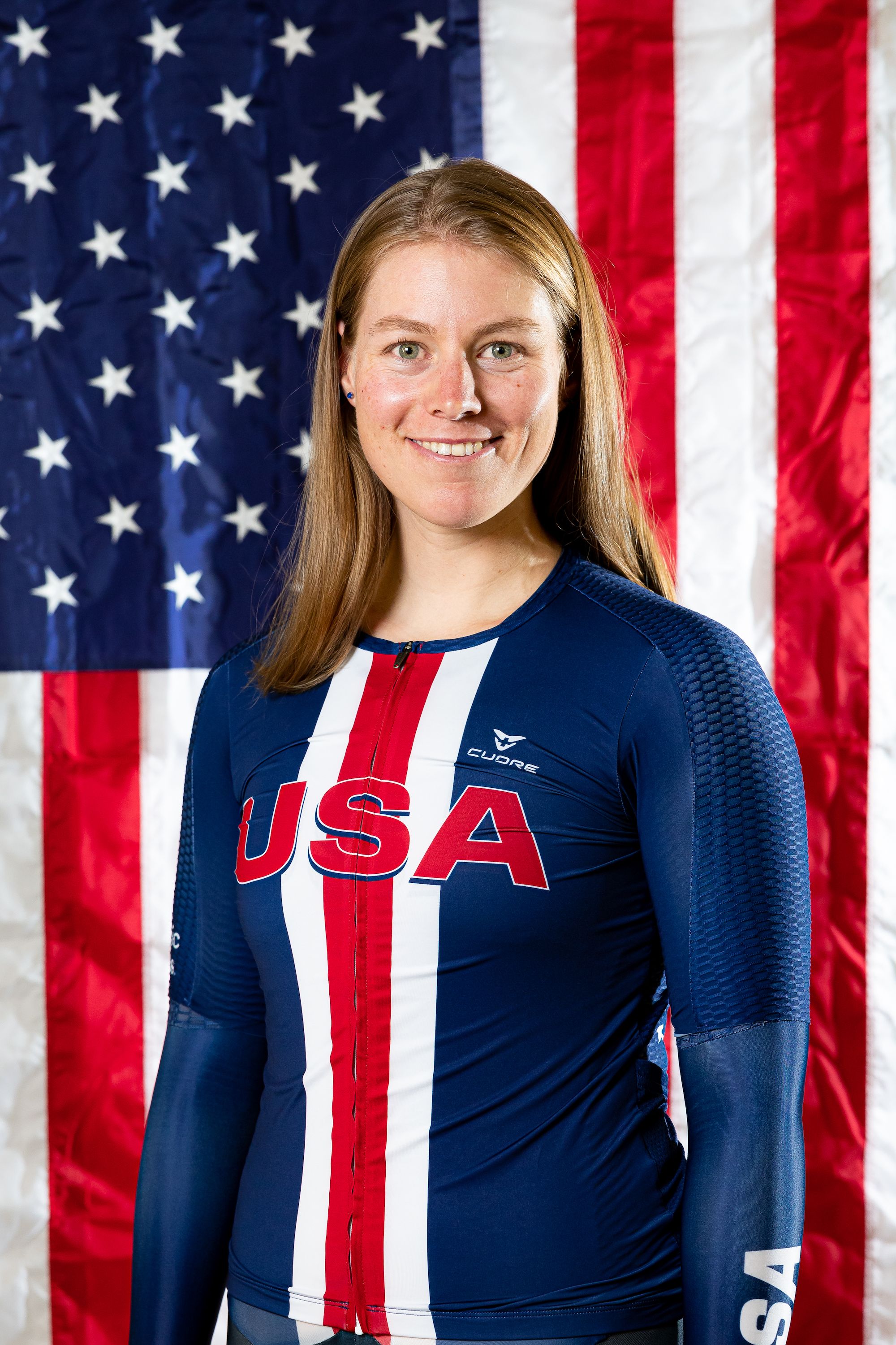 Headshot of Team USA cyclist Jennifer Valente in front of an American flag.
