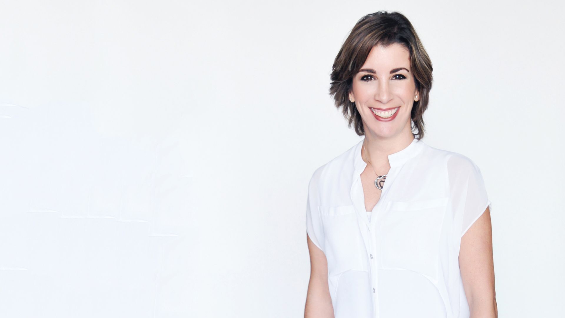 Andreina Pradas smiles brightly while wearing a bright white shirt against a white background.