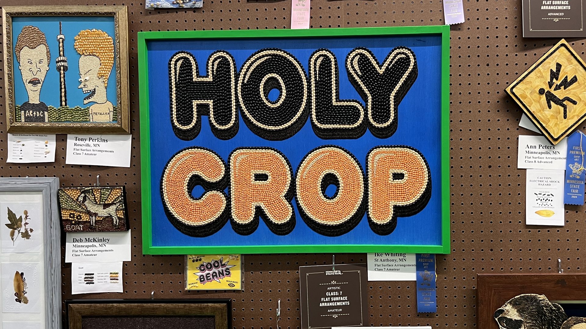 A piece of seed art reading "Holy Crap" in large bubble letters on a blue background