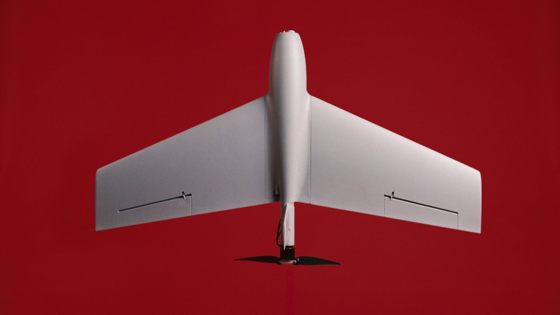 Top-down view of a white drone with a tall, rounded nose and broad swept wings, set against a solid red background.