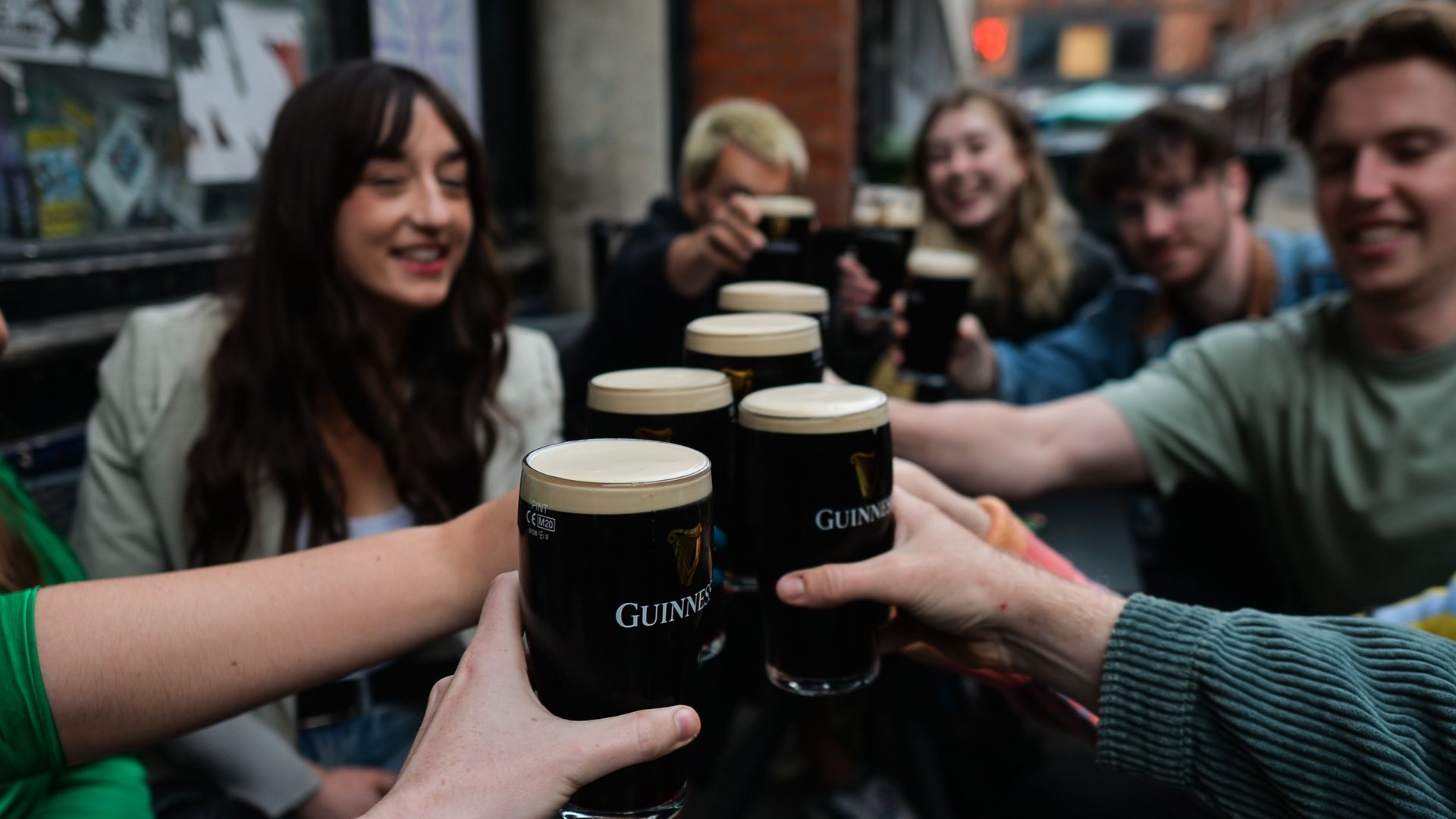 A group of young adults toast pints of Guinness beer. 