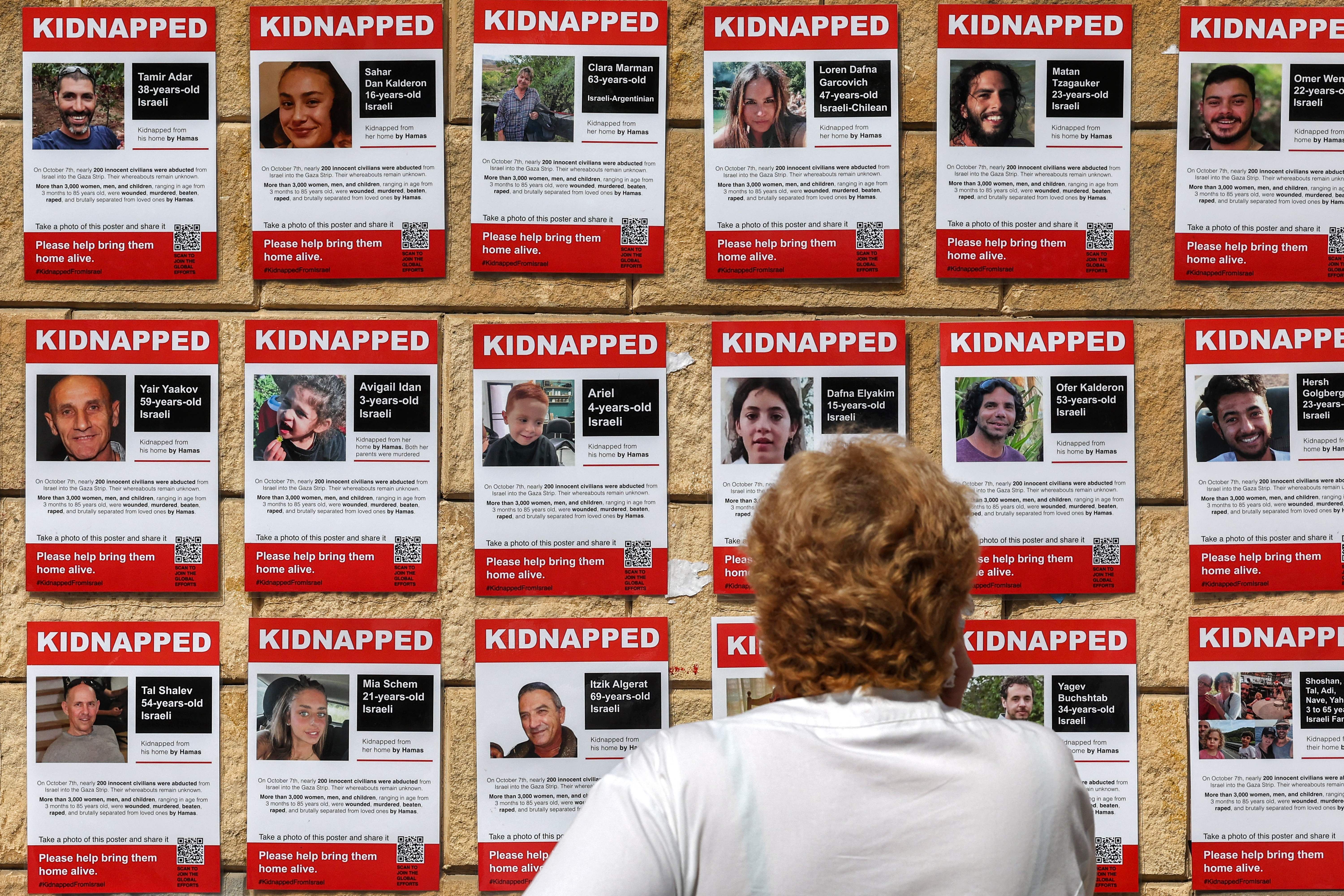 A woman stands in front of posters showing images of the kidnapped hostages. 