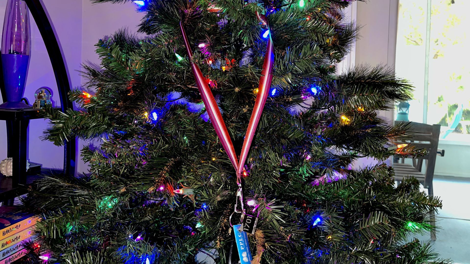 Selene's lesbian flag lanyard hangs on a Christmas tree with lights.