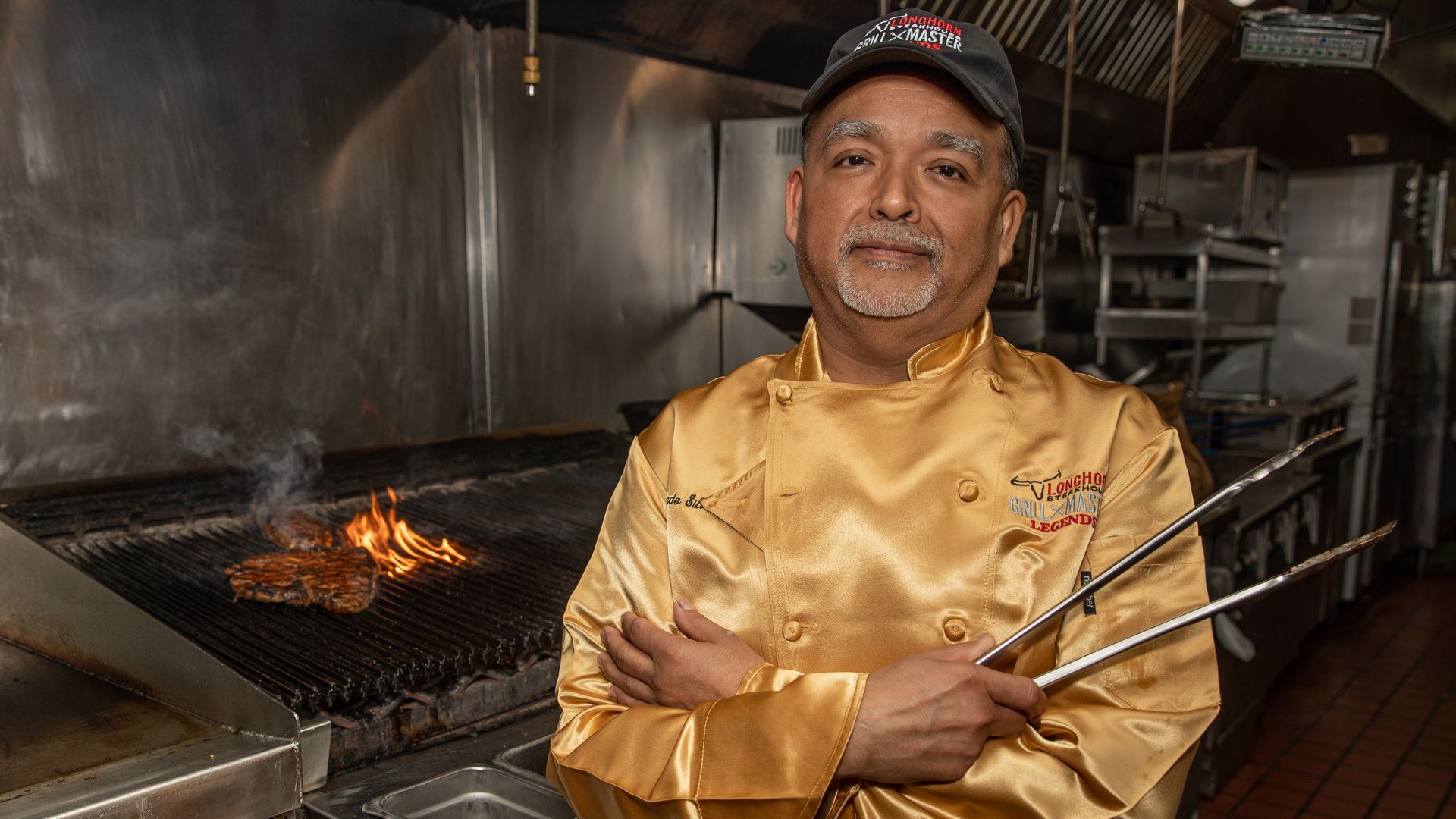 Santos wearing his gold jacket and standing in front of a grill with a steak on it