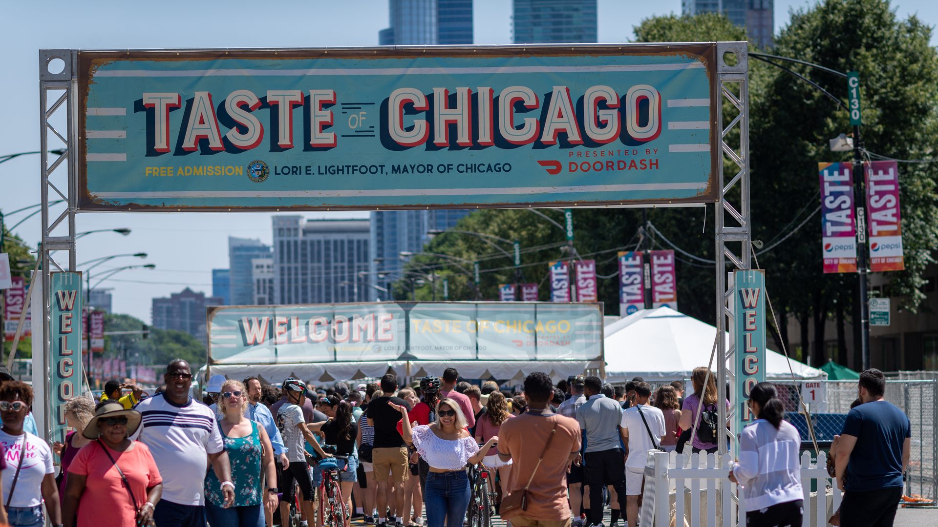 People walk under a blue banner that reads "Taste of Chicago"