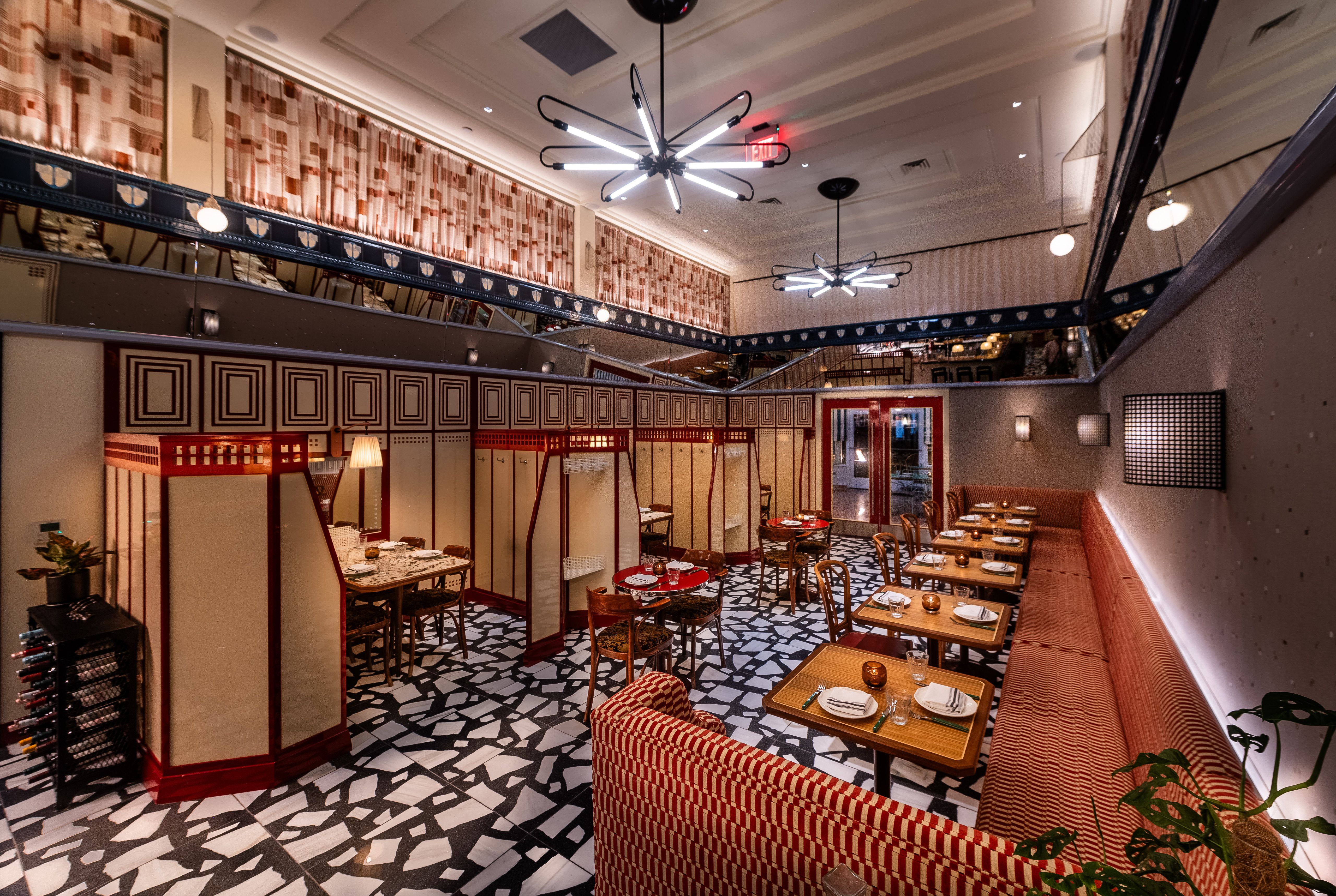 Interior of a retro restaurant with a black-and-white mosaic floor, red checkered booths, and wooden tables set with plates. Modern starburst ceiling lights and patterned curtains.