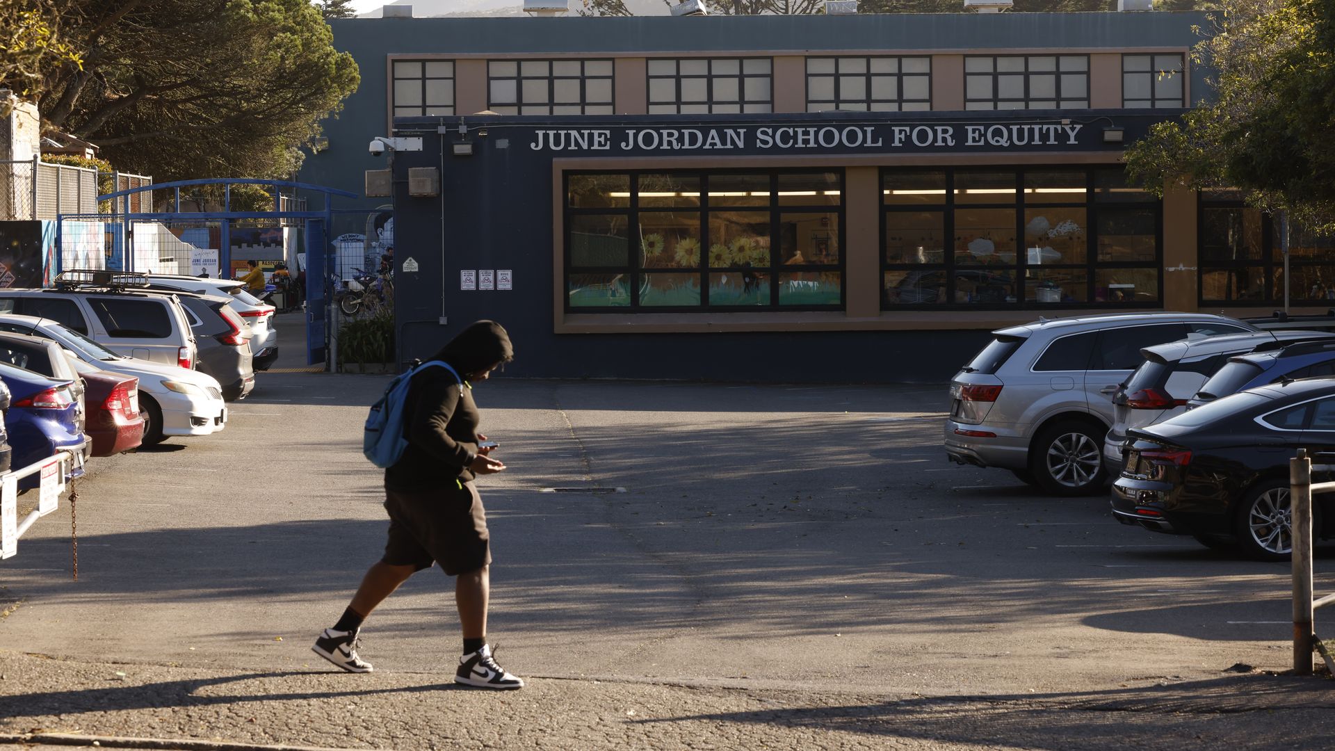 Photo of a student walking across a parking lot in front of the June Jordan School for Equity entrance