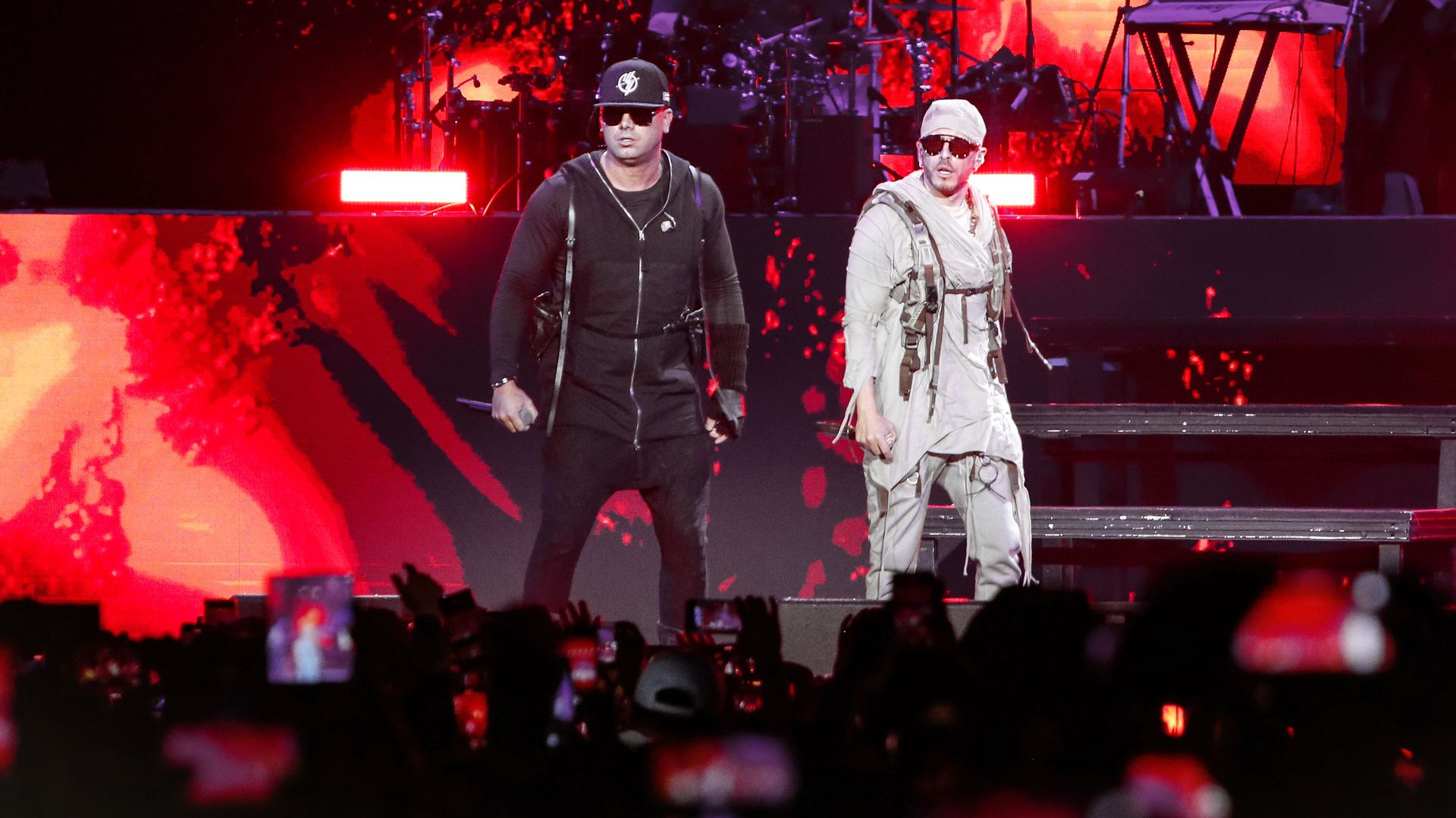 Reggaeton artists Wisin y Yandel onstage with red flame-like optics in the background.