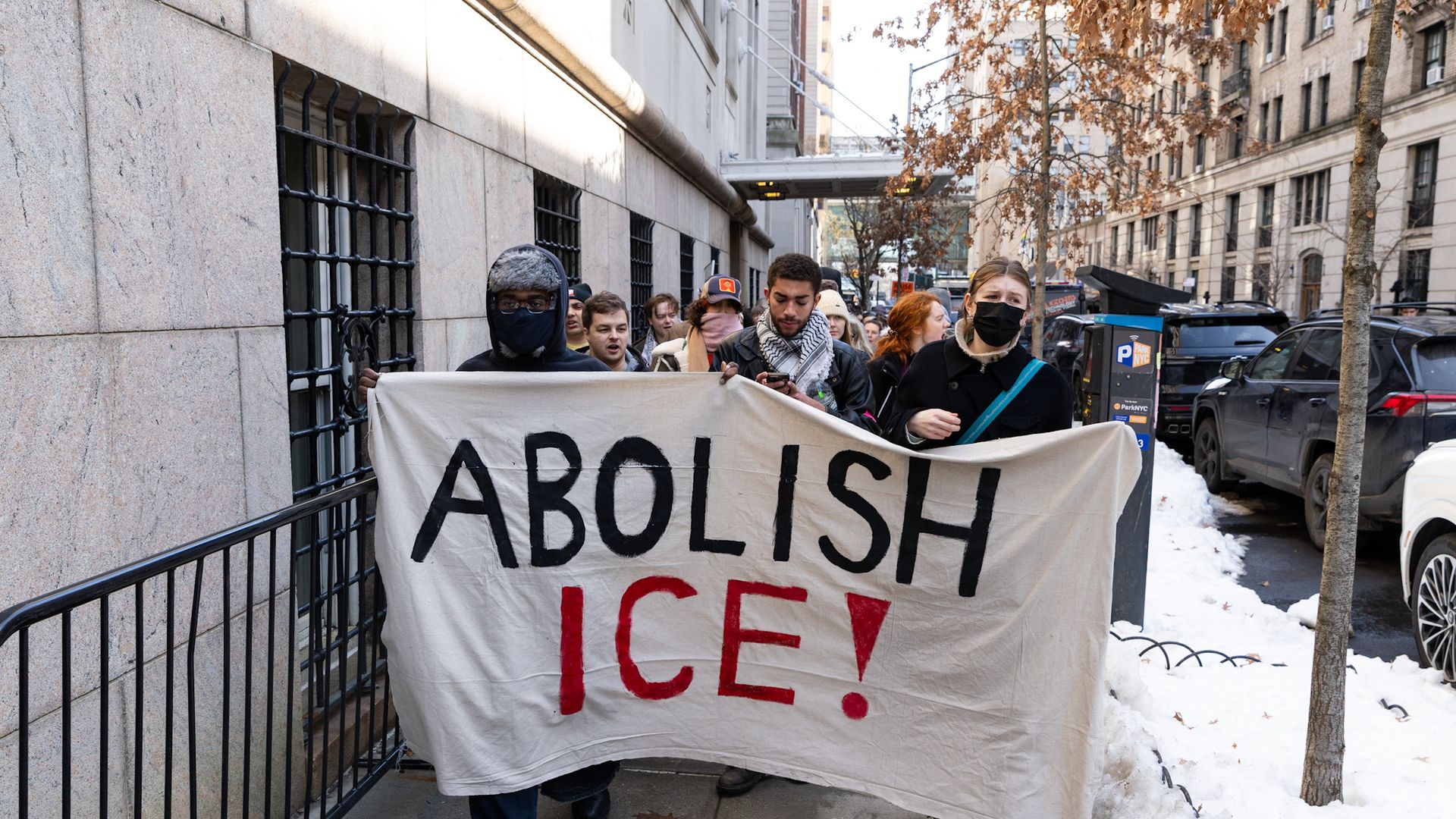 A group of protesters marching outside on the streets holding a large sign that reads "ABOLISH ICE"