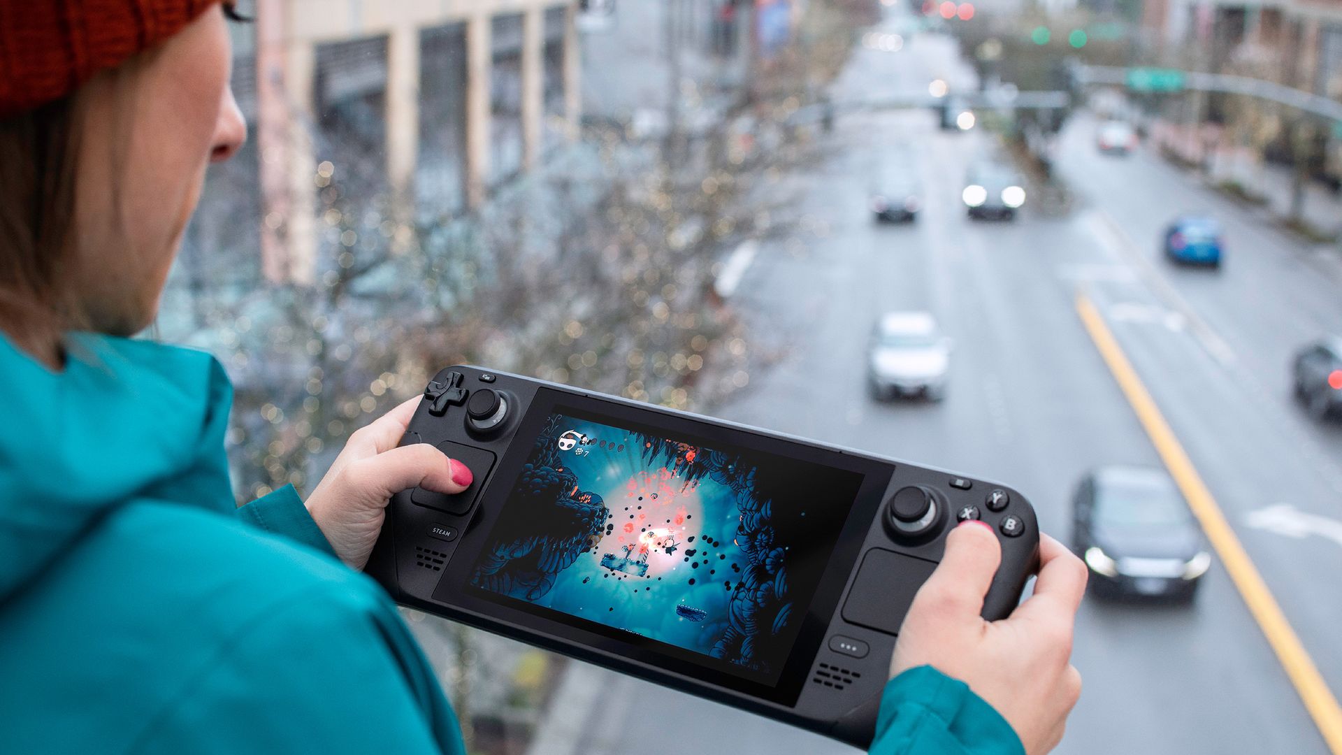 A woman plays a handheld gaming device while standing near a busy highway.