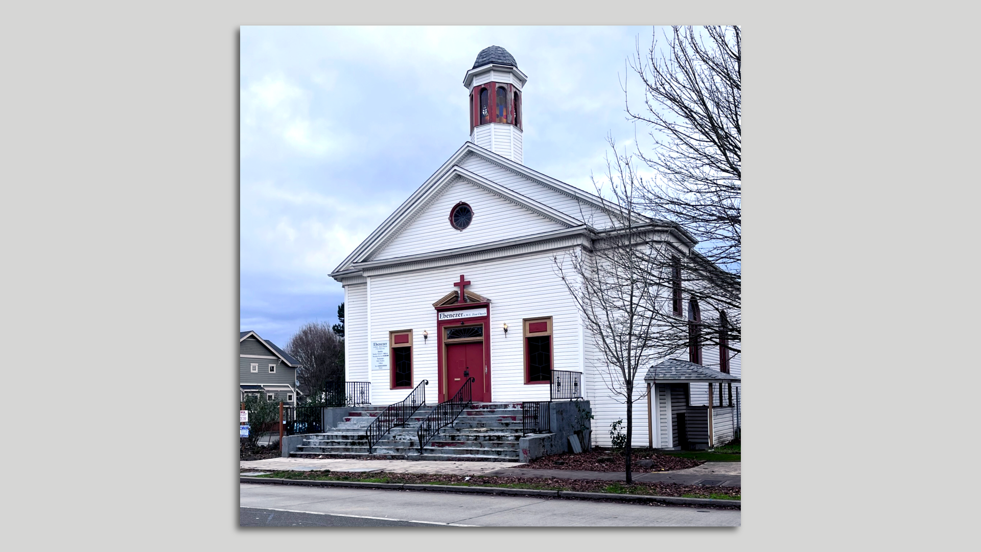 A photo of a white church with pointed roof and tower emerging from roof with a red door, mounted on a gray background.