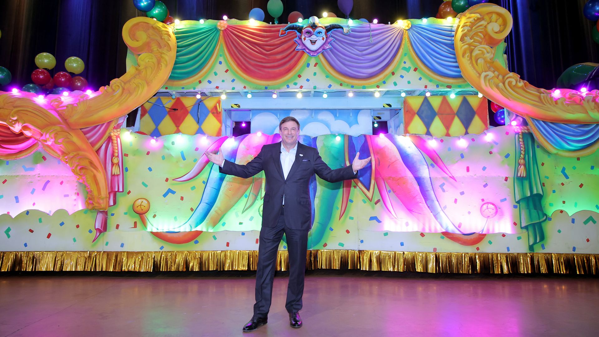 Todd Graves gestures his arms out as he stands in front of a Mardi Gras float.